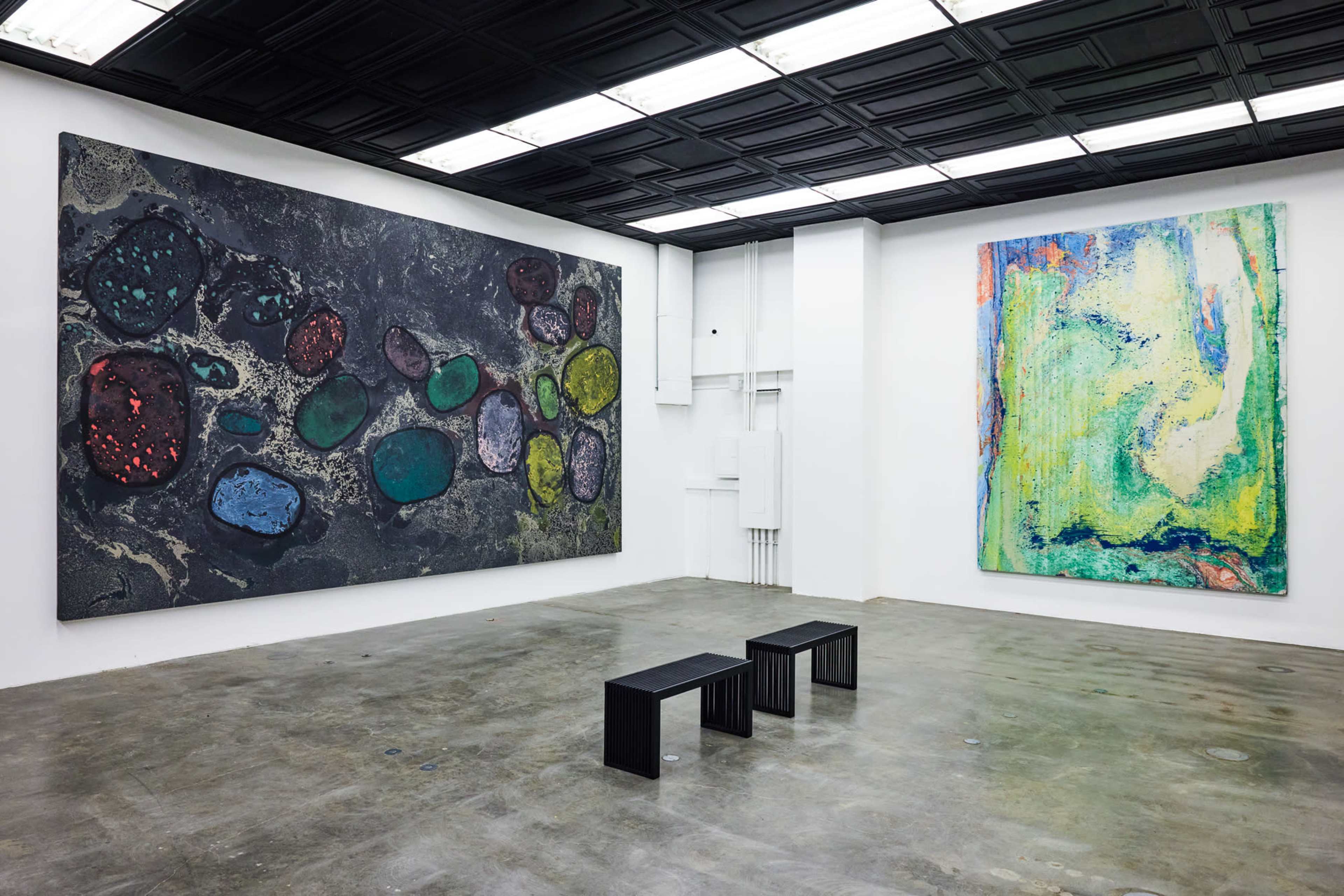 The image shows a modern art gallery with two large abstract paintings on the walls and three black benches arranged in the center of the room.