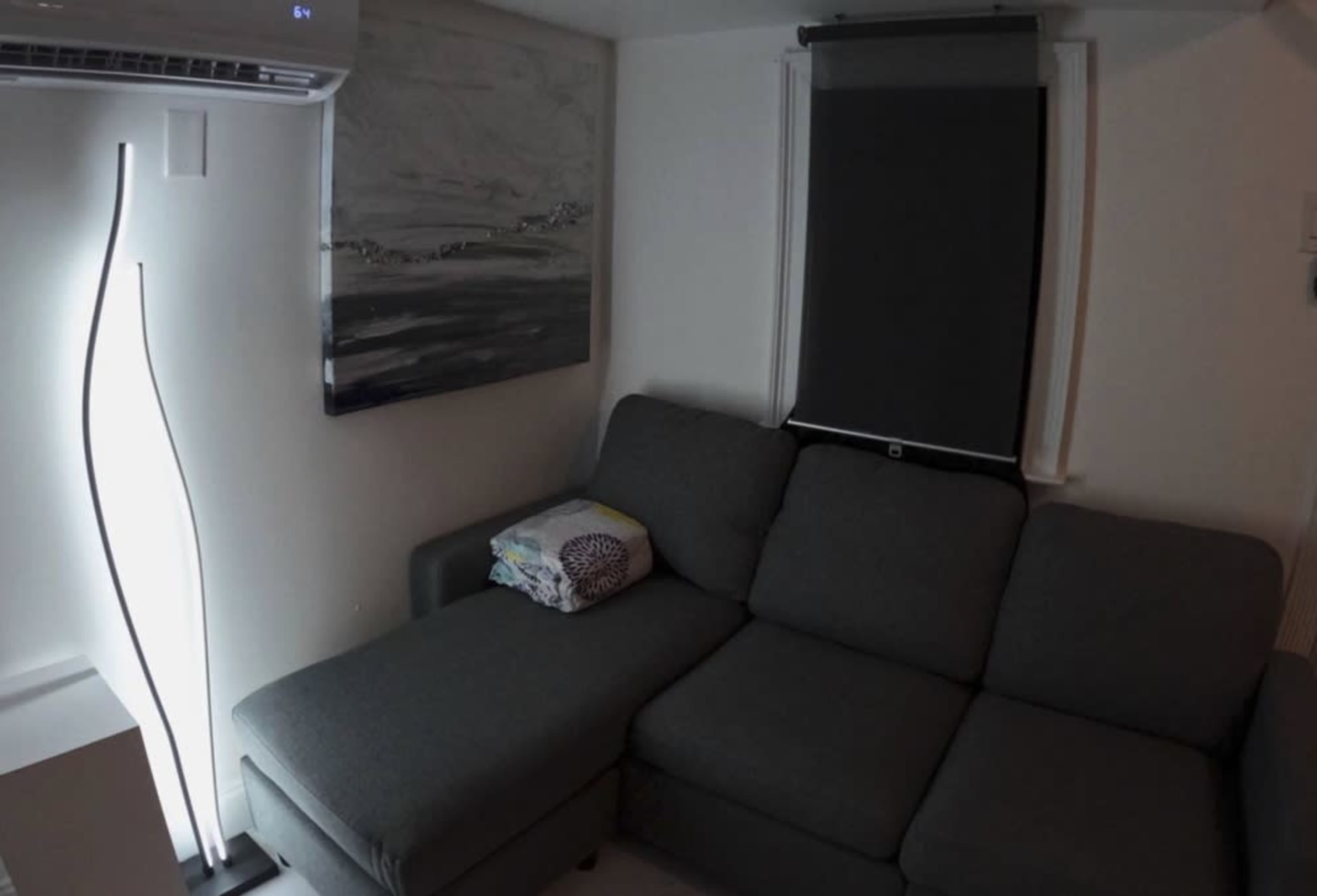 A gray sectional sofa is positioned in a room next to a wall-mounted painting and a standing lamp.