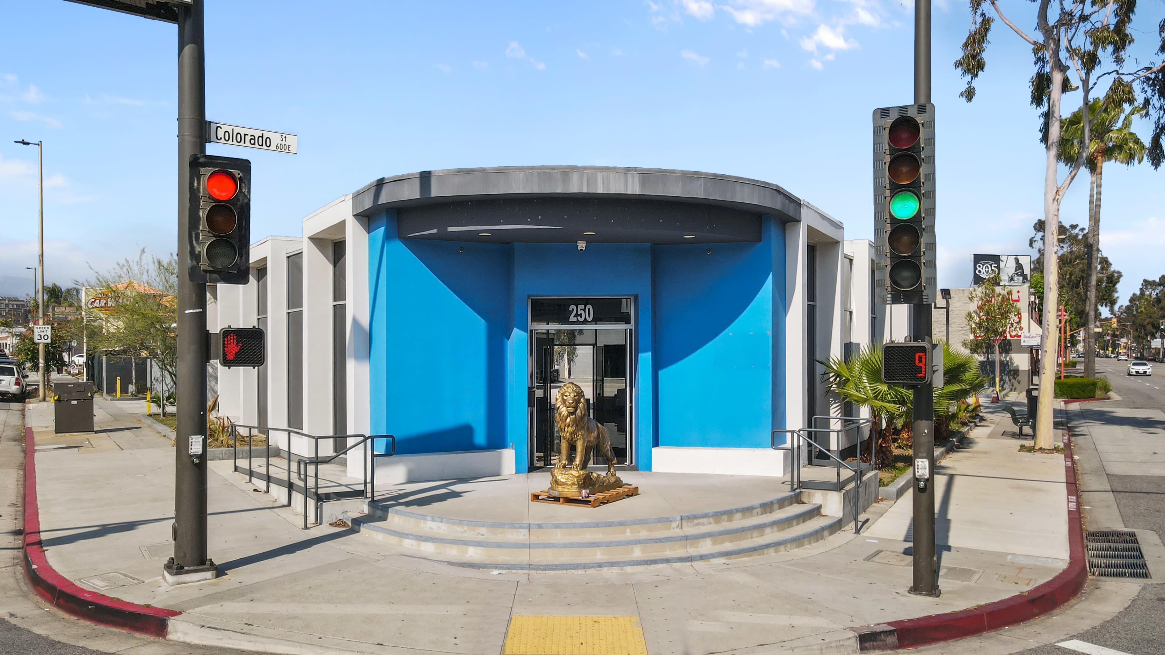 A modern building with a blue facade and a golden lion statue at its entrance, situated at an intersection with traffic lights.