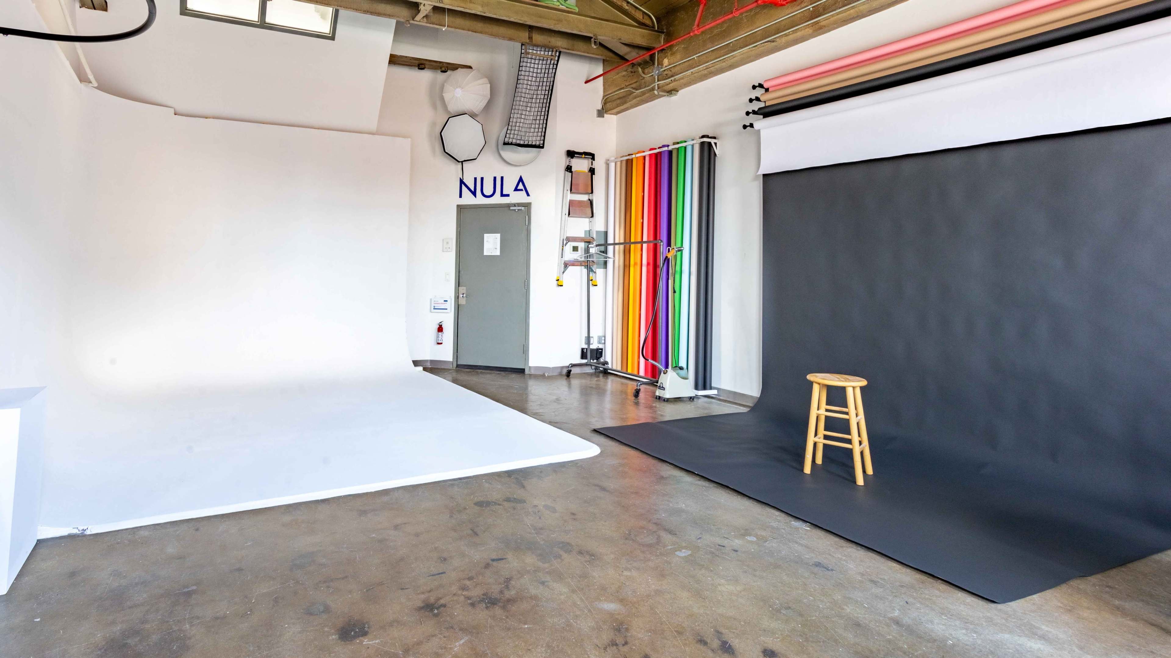 The image shows a photography studio with a white backdrop on one side, a black backdrop on the other, and a wooden stool placed in front of the black backdrop.