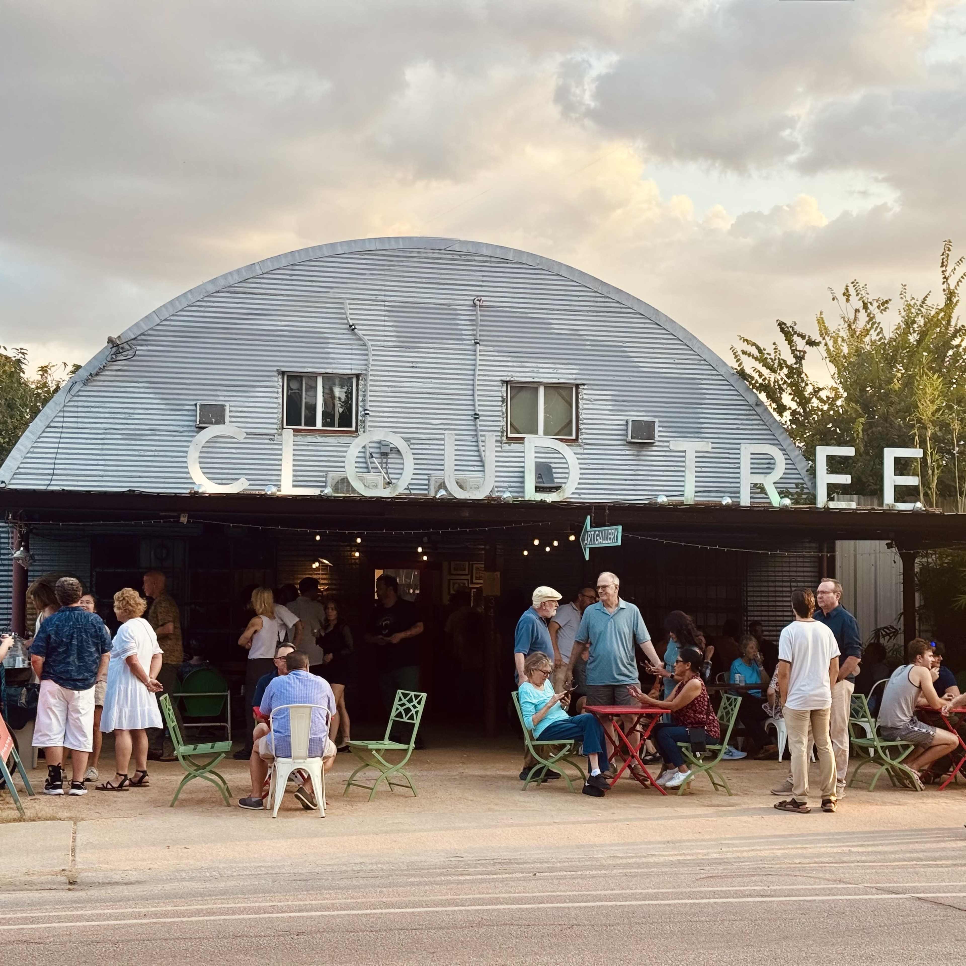 The image shows a crowd of people gathered outside a restaurant called "Cloud Tree," with seating and a metal exterior under a cloudy sky.