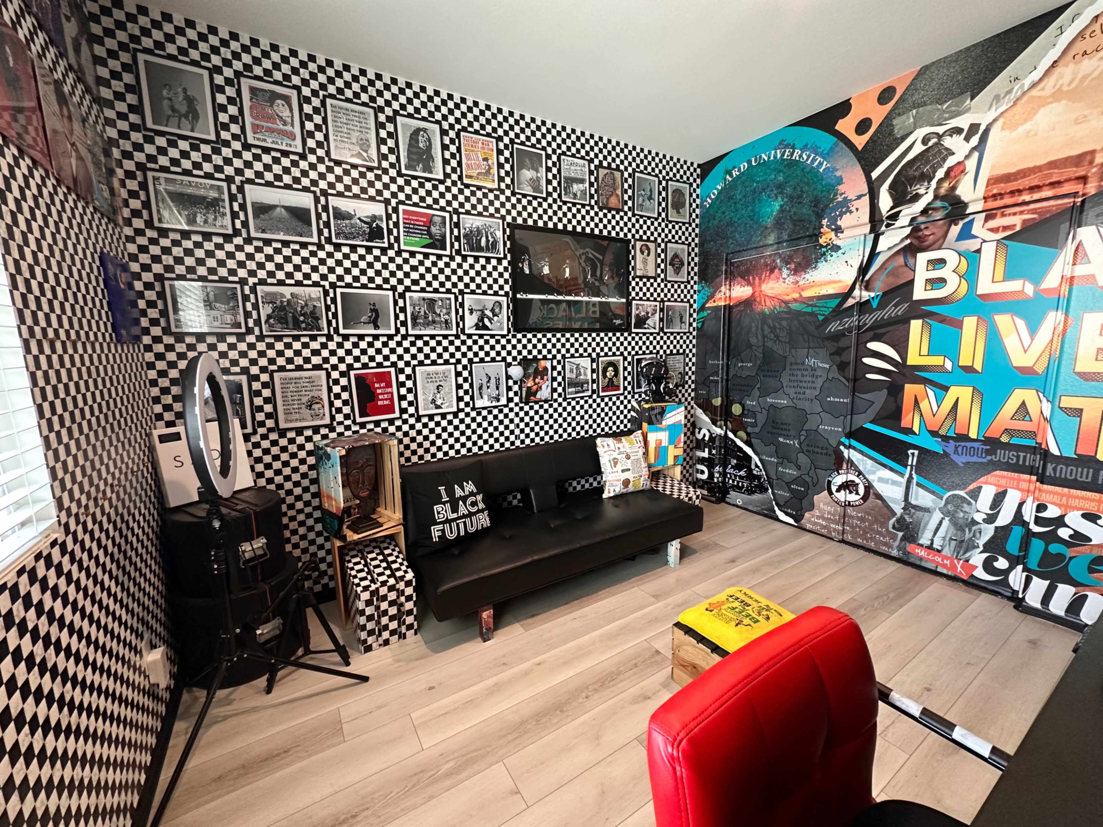 The room features a black and white checkered wall design, adorned with various framed photographs, and a large mural with the phrases "BLACK LIVES MATTER" and "I AM BLACK FUTURE."