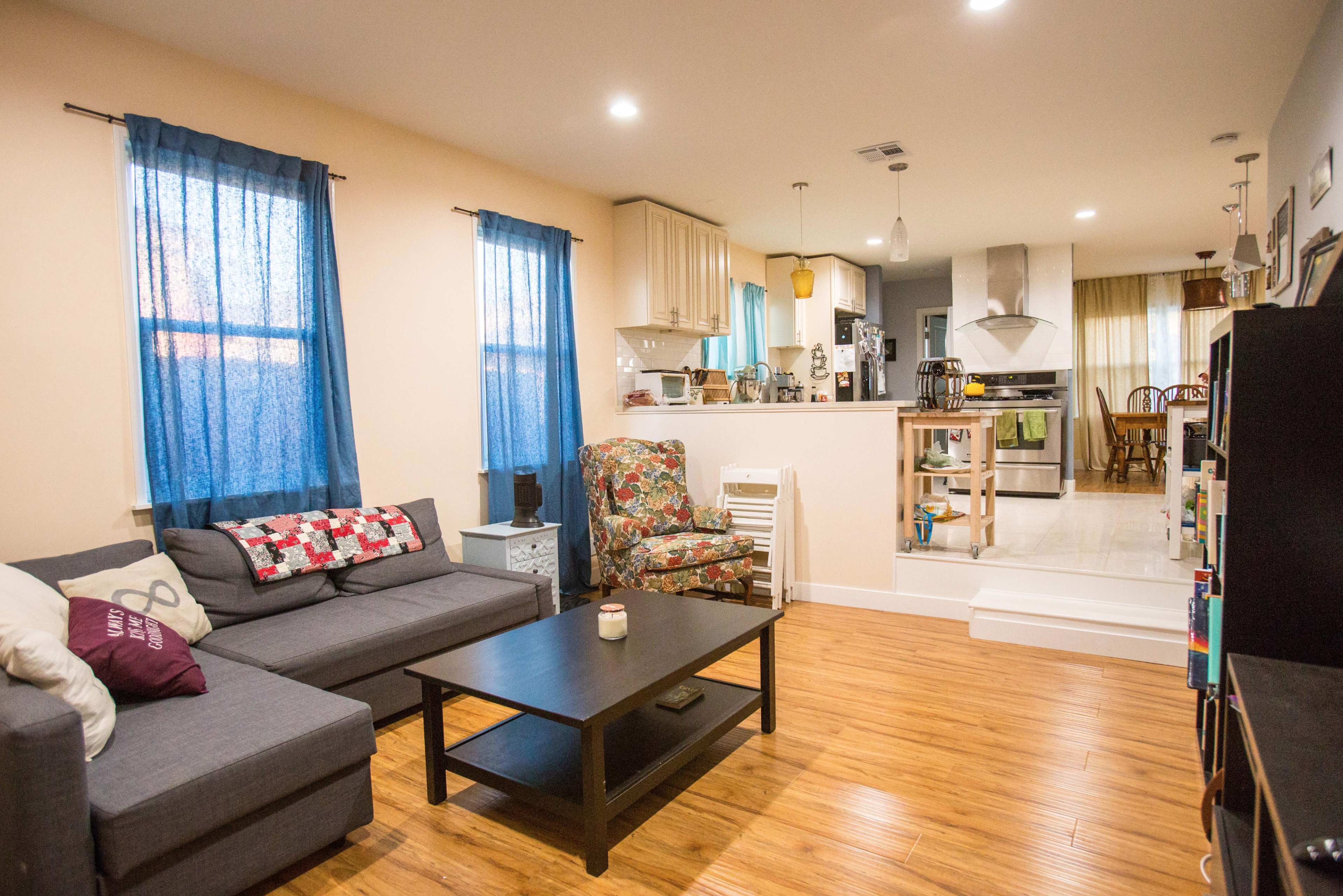 A modern living room featuring a gray couch, a black coffee table, and a cozy chair, with a partially visible kitchen in the background.