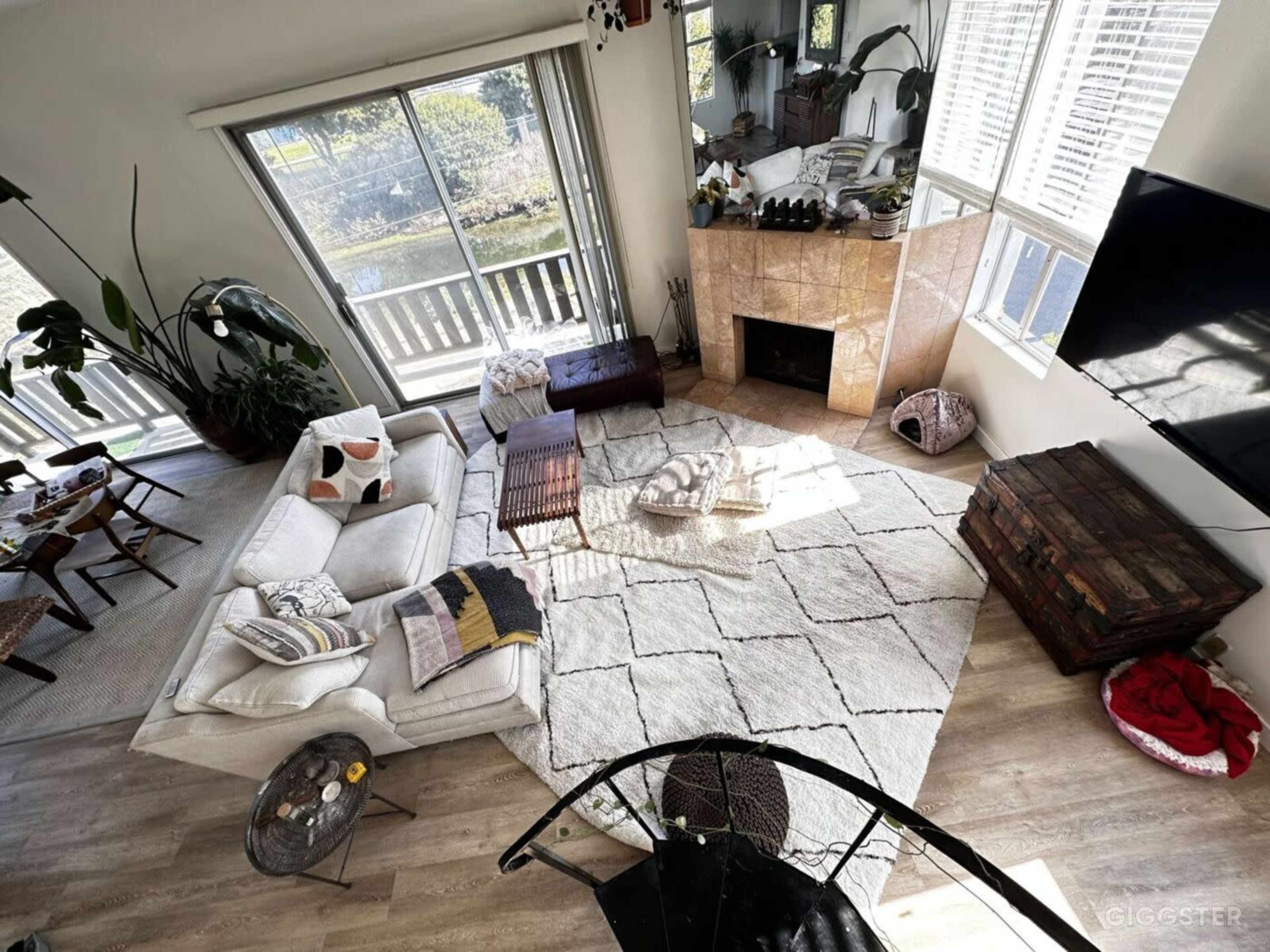 The image shows a spacious living room with a large sectional sofa, a coffee table, and a fireplace, illuminated by natural light from windows overlooking a garden.