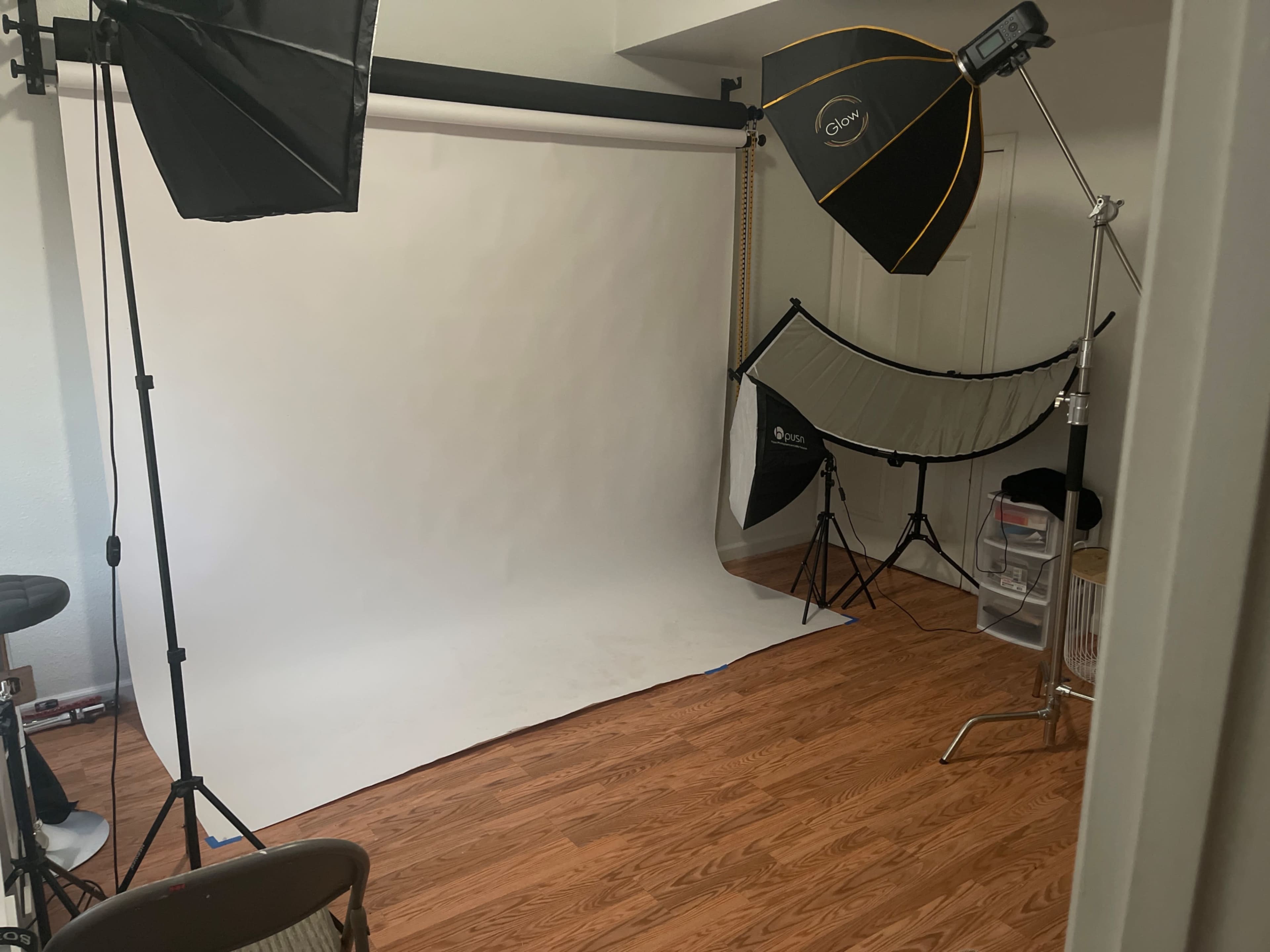 A photography studio setup with a white backdrop, multiple light sources, and wooden flooring.
