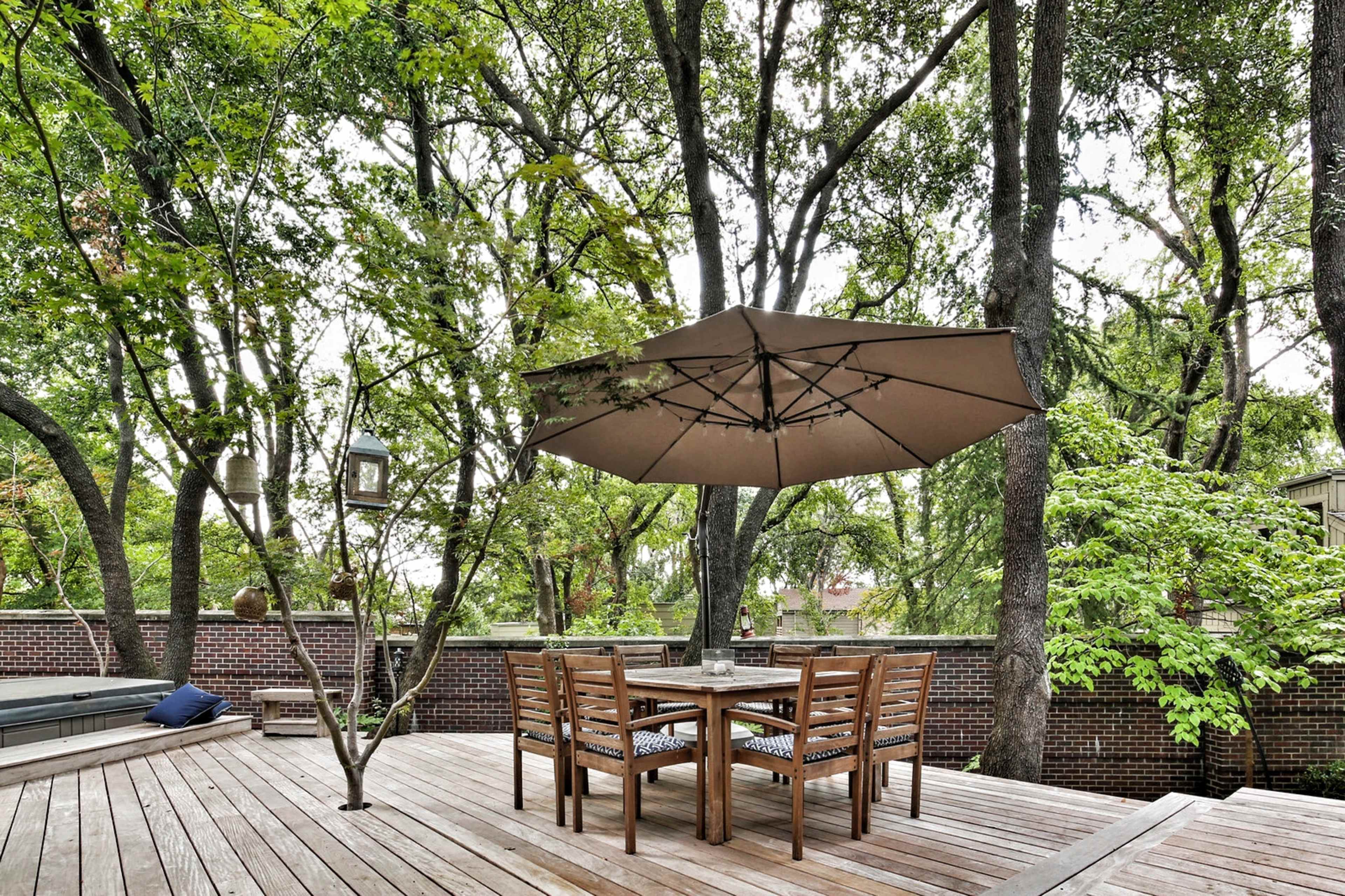 A wooden deck features a table and chairs under a large umbrella, surrounded by trees and greenery.