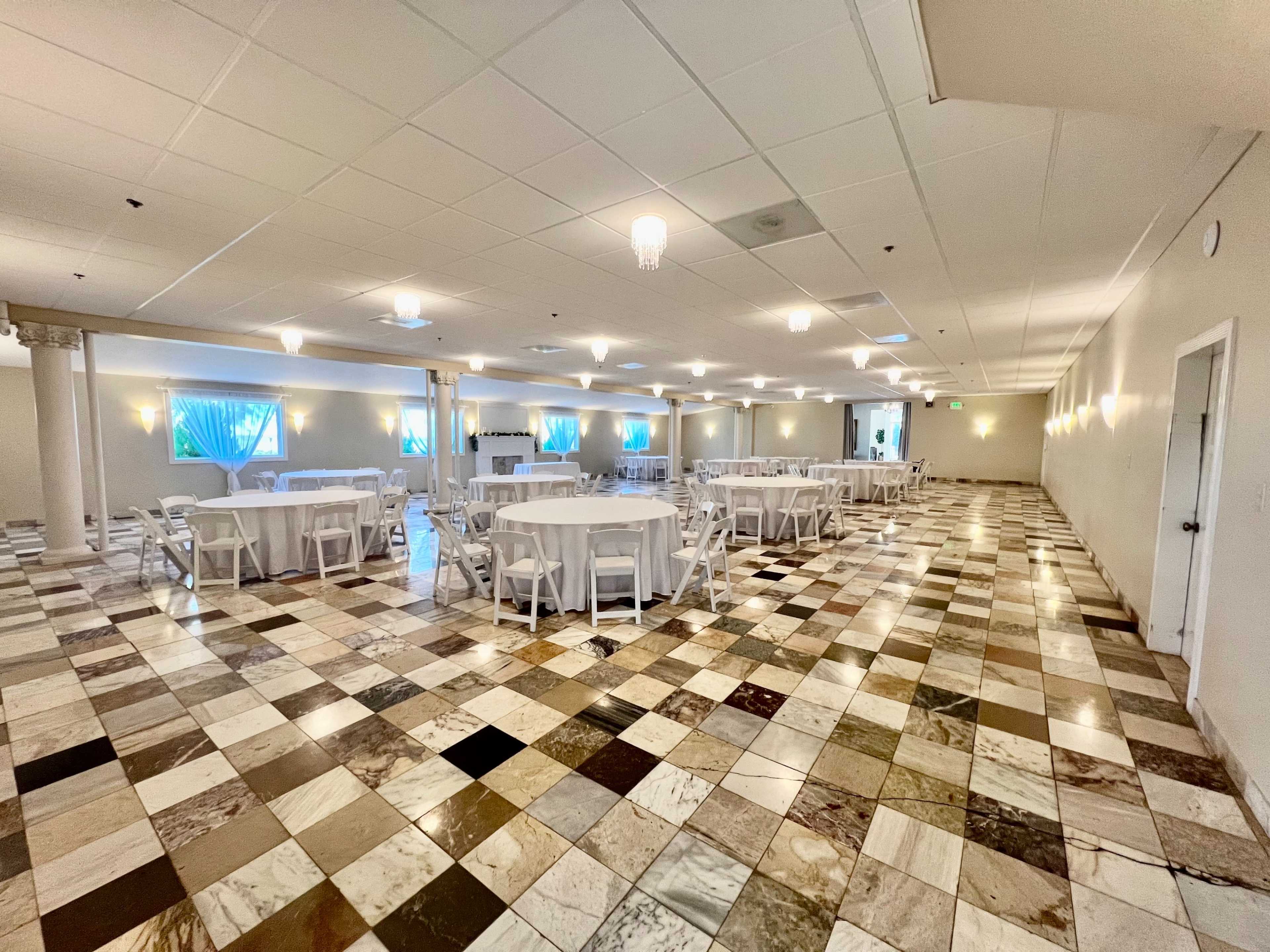 A spacious event hall with a tiled floor and multiple round tables arranged in rows.