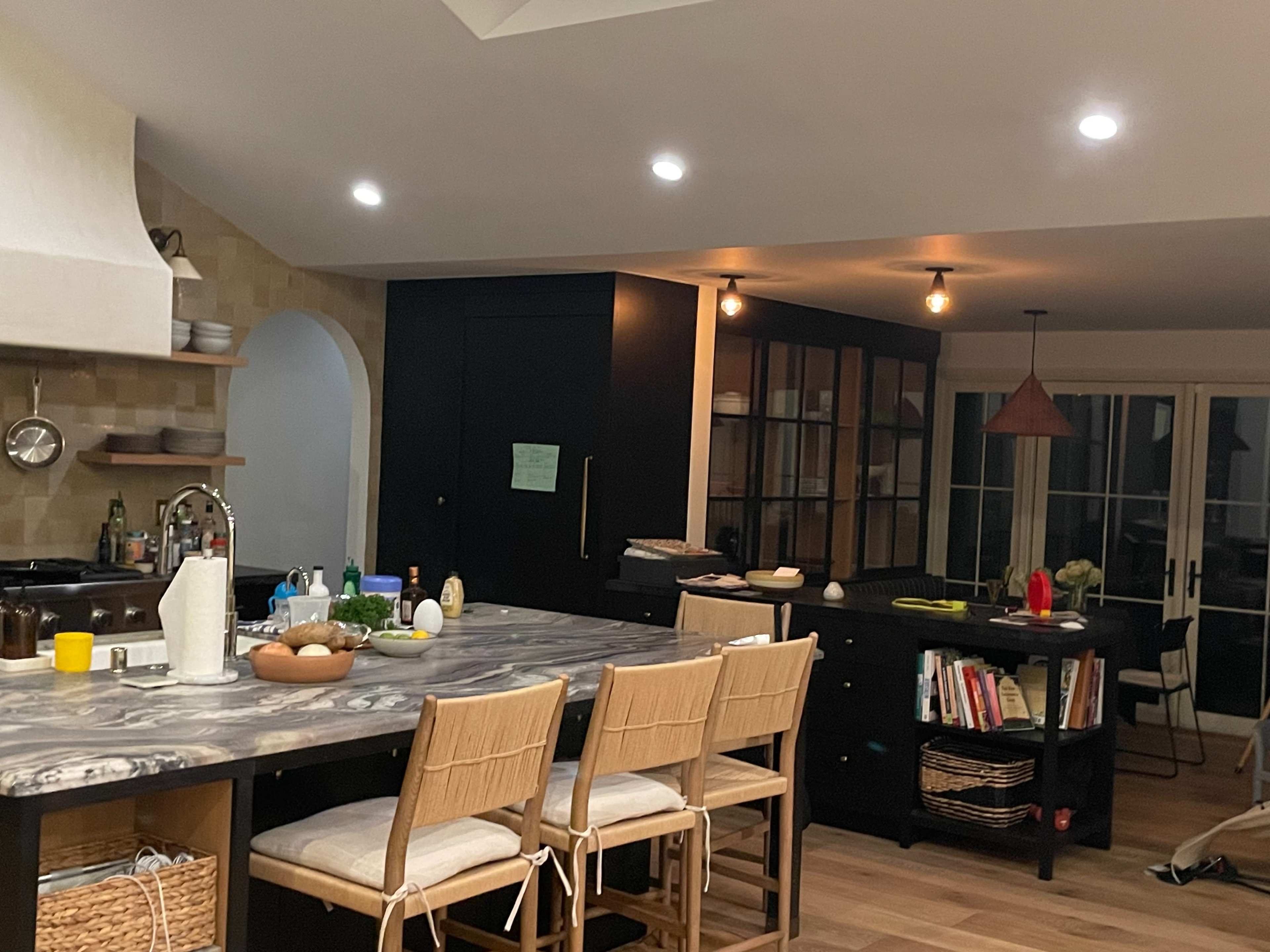 The image shows a modern kitchen with a large central island, bar stools, and various kitchen appliances and accessories.