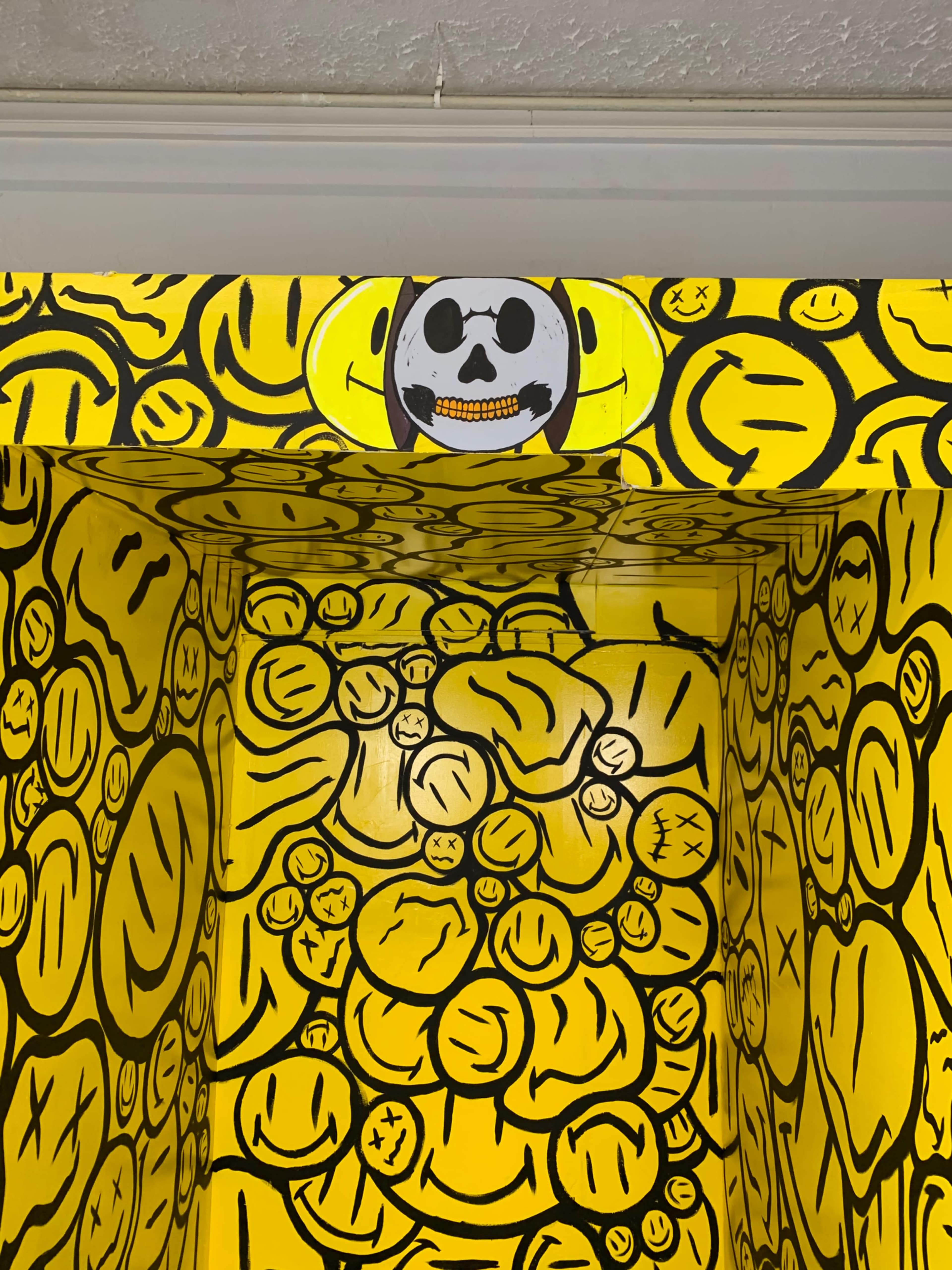 A brightly painted room with yellow walls covered in various smiley faces and a skull with a smile above.