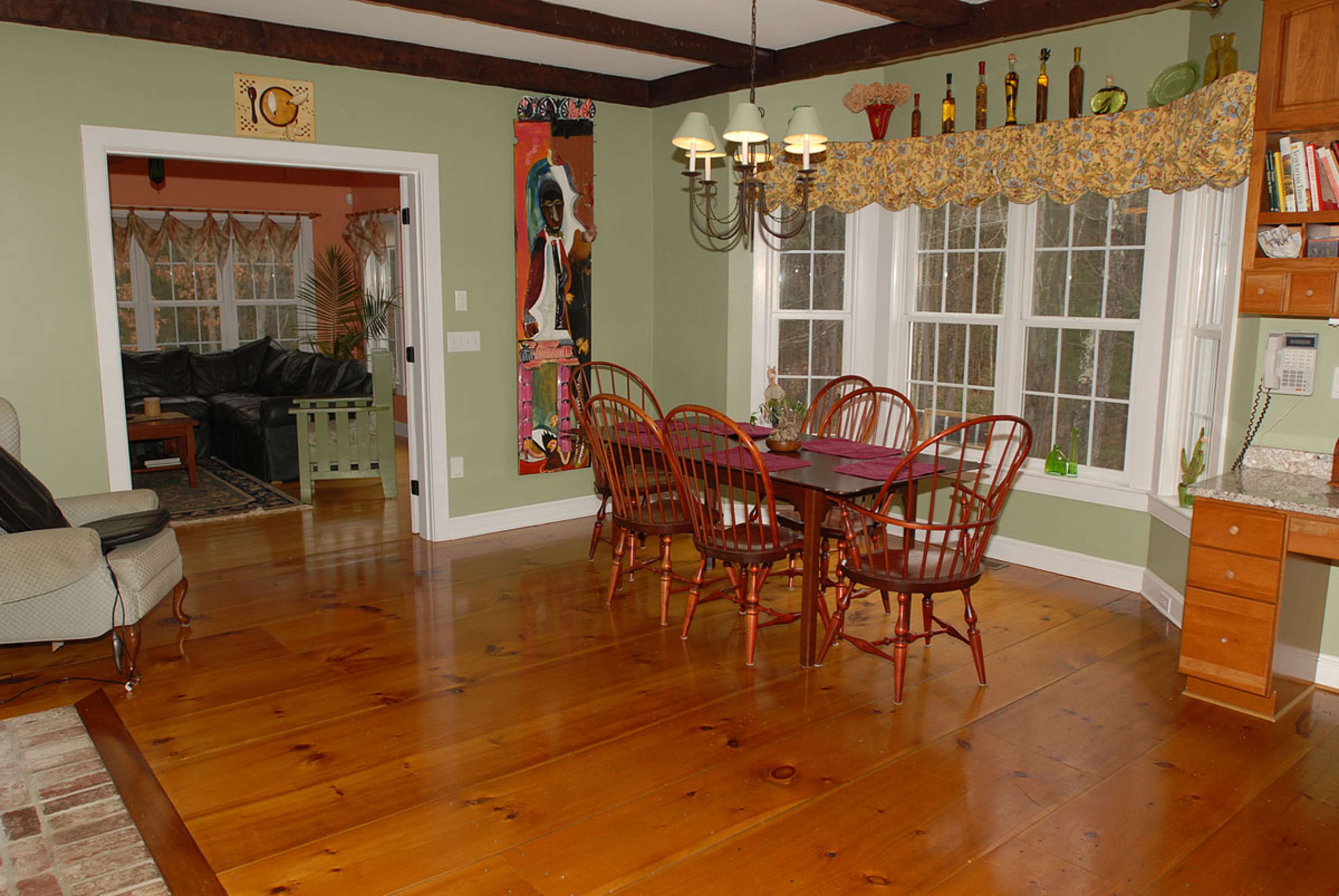 A dining area features a wooden table surrounded by chairs, with large windows and a doorway leading to another room.