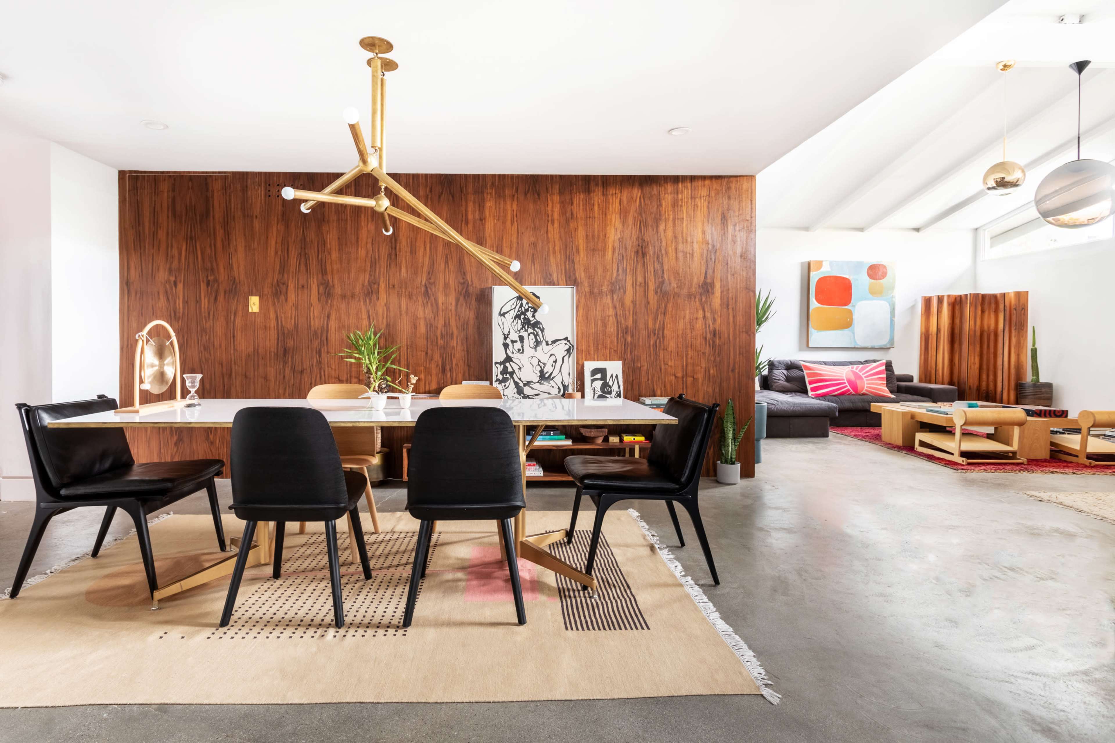 A dining area features a large table surrounded by black chairs, with wooden wall paneling and modern artwork in the background.