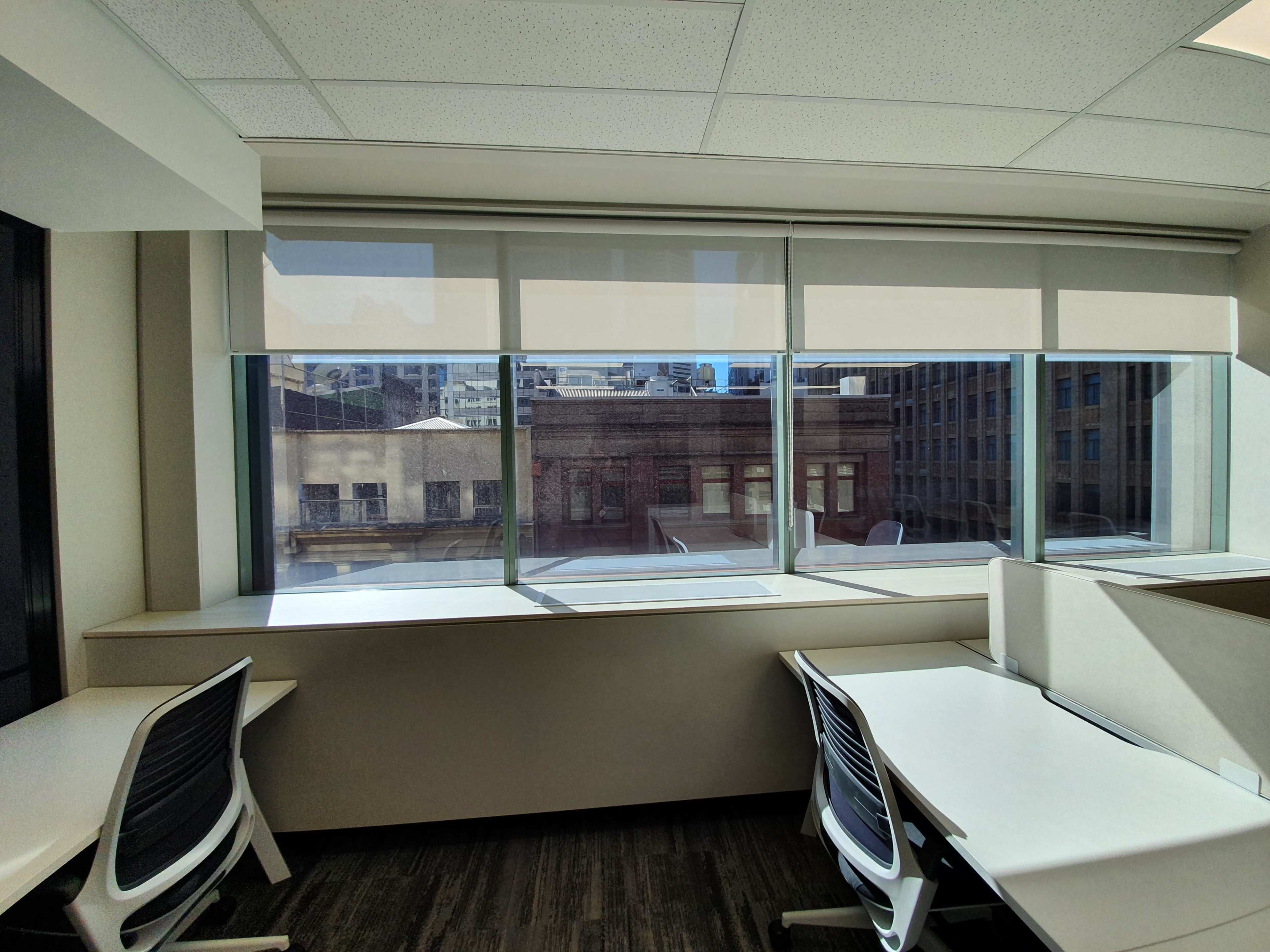 The image shows a modern office space with large windows, white desks, and ergonomic chairs.
