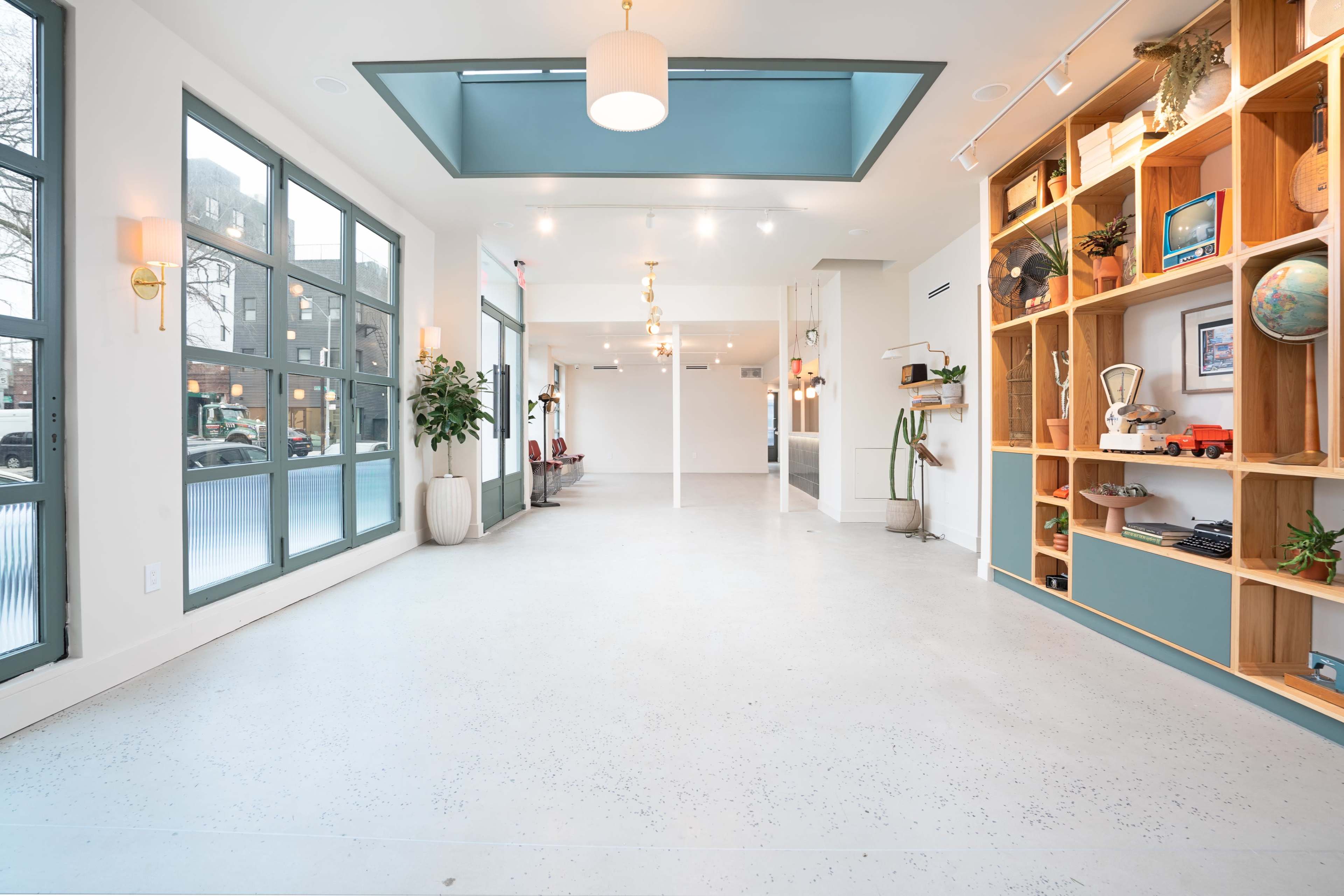 A bright, spacious interior with large windows, a light-colored floor, and a wooden shelving unit displaying various decorative items.