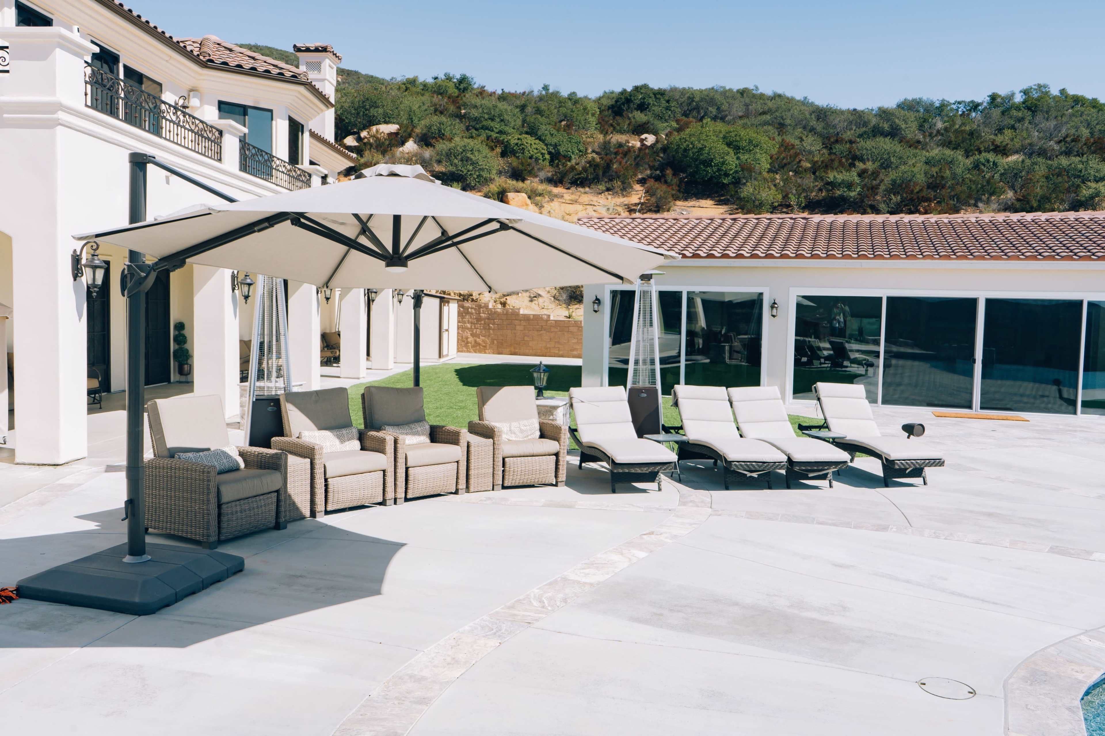 A spacious outdoor area features a set of wicker chairs and a large umbrella near a swimming pool and lounge chairs.