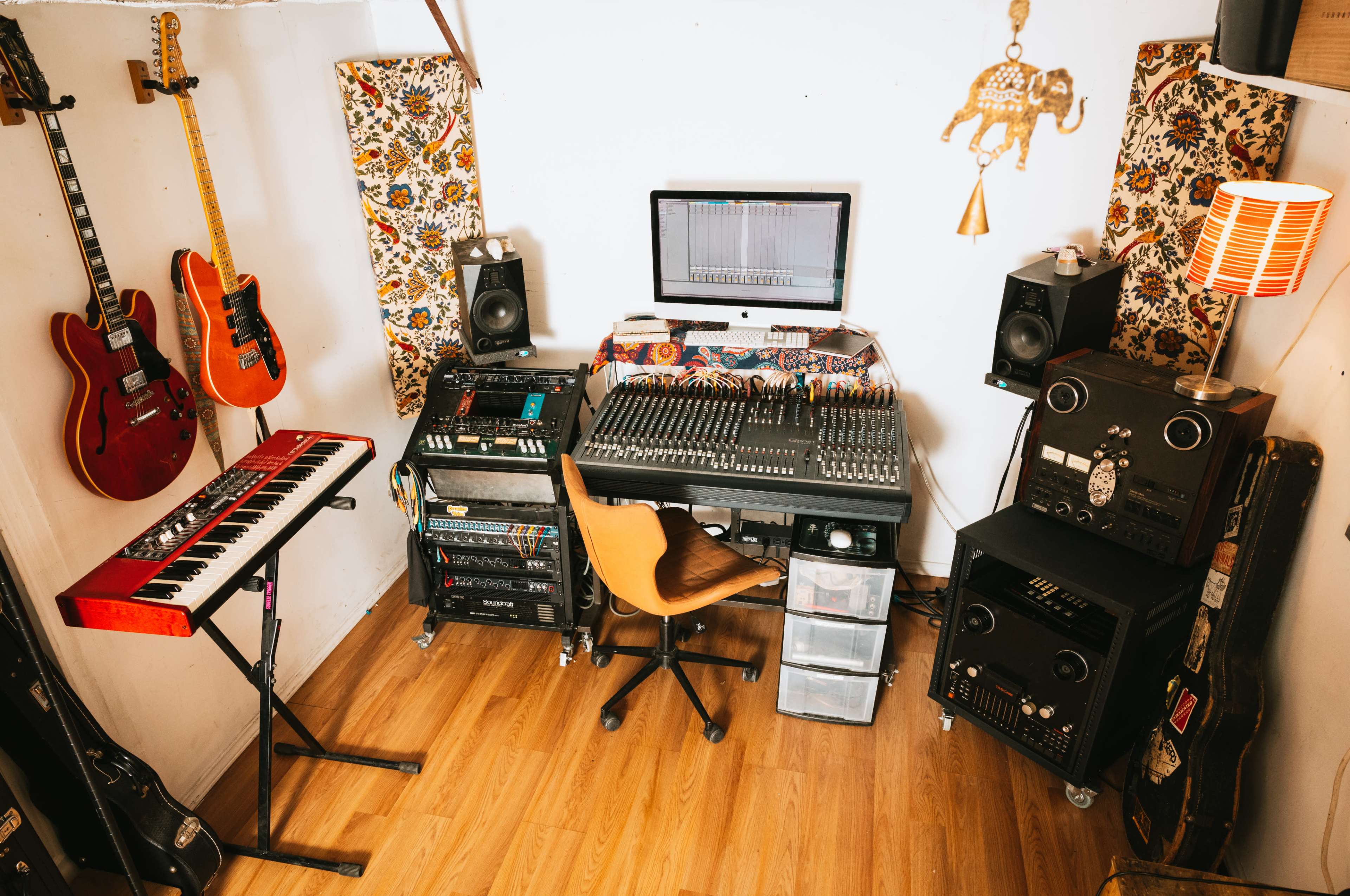 A music recording studio featuring guitars, a keyboard, a mixing desk, and various audio equipment arranged around a computer monitor.