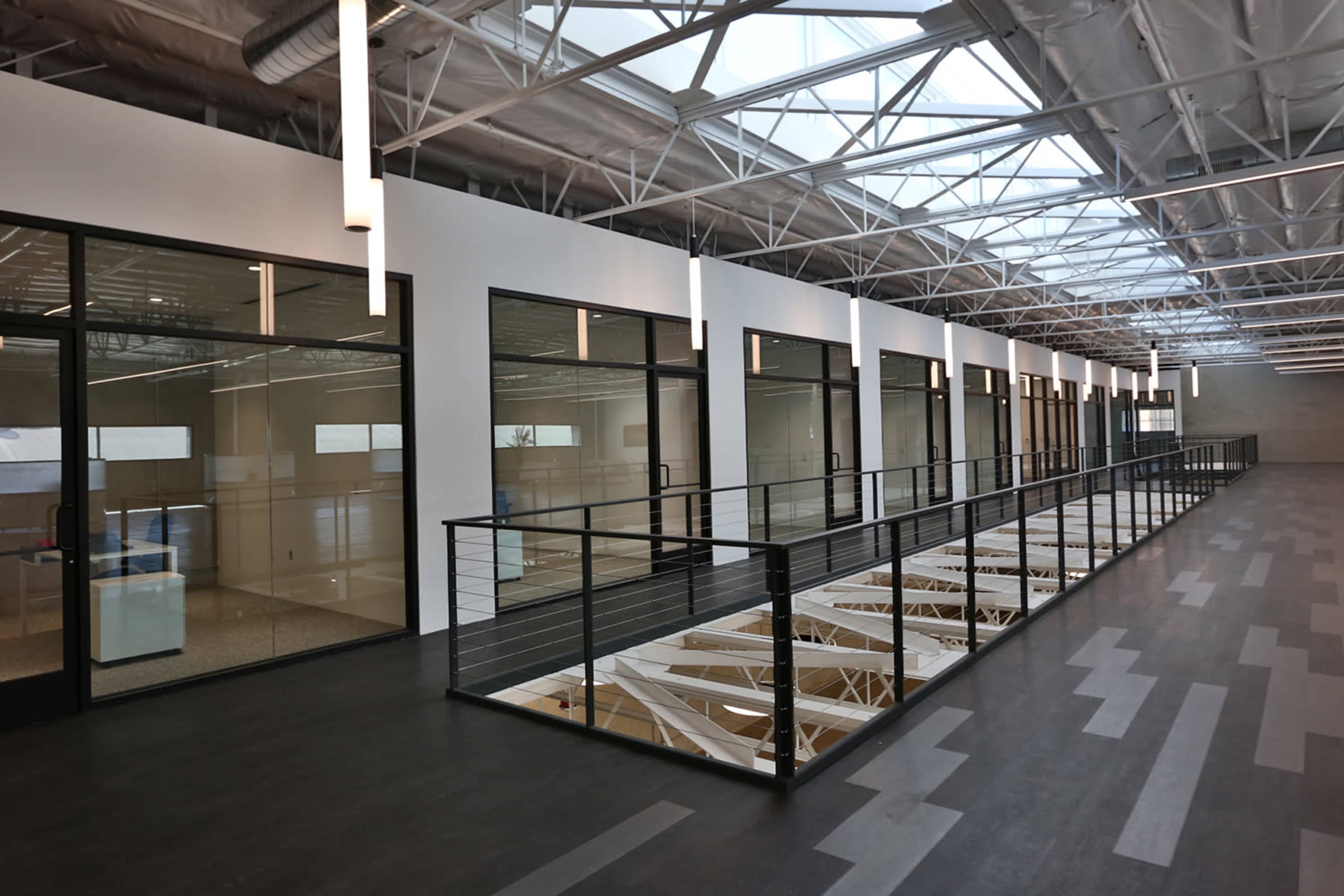 A modern interior hallway with large windows and a glass railing overlooking an open space below.