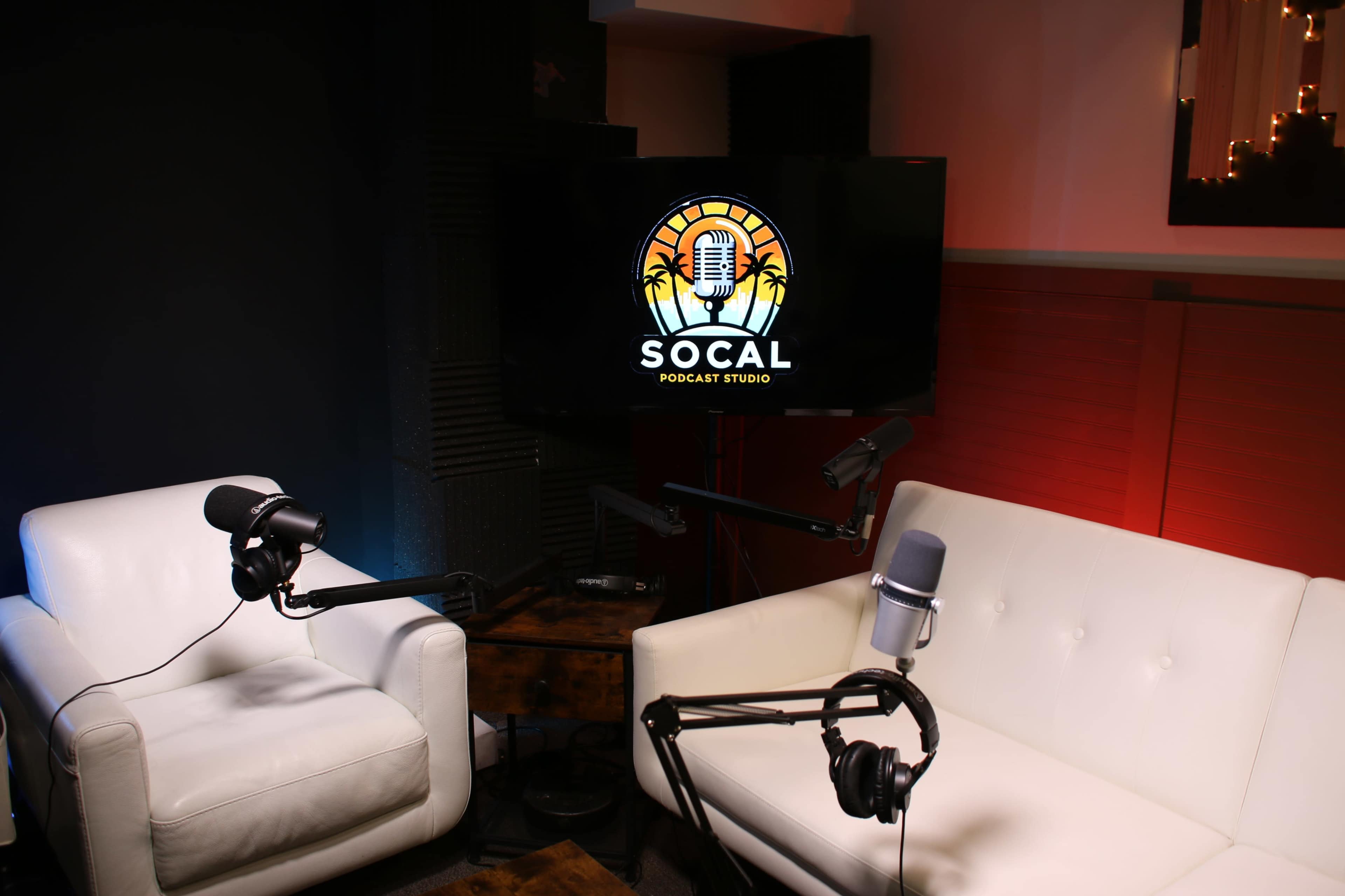 A podcast studio featuring two white chairs and microphones facing a television screen displaying the "SOCAL PODCAST STUDIO" logo.