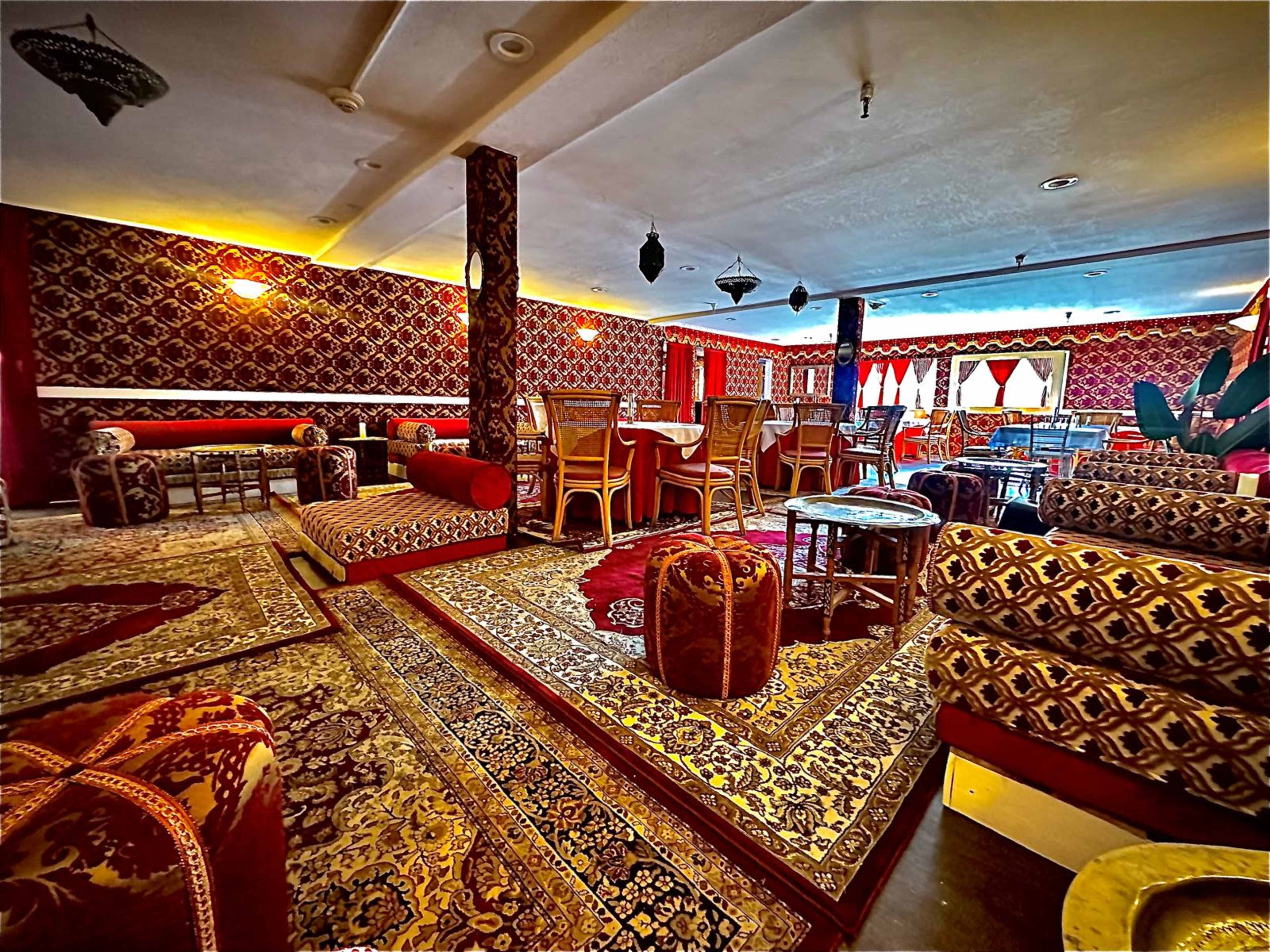 The image shows an elegantly decorated lounge area featuring patterned rugs, plush seating, and intricate wall designs.