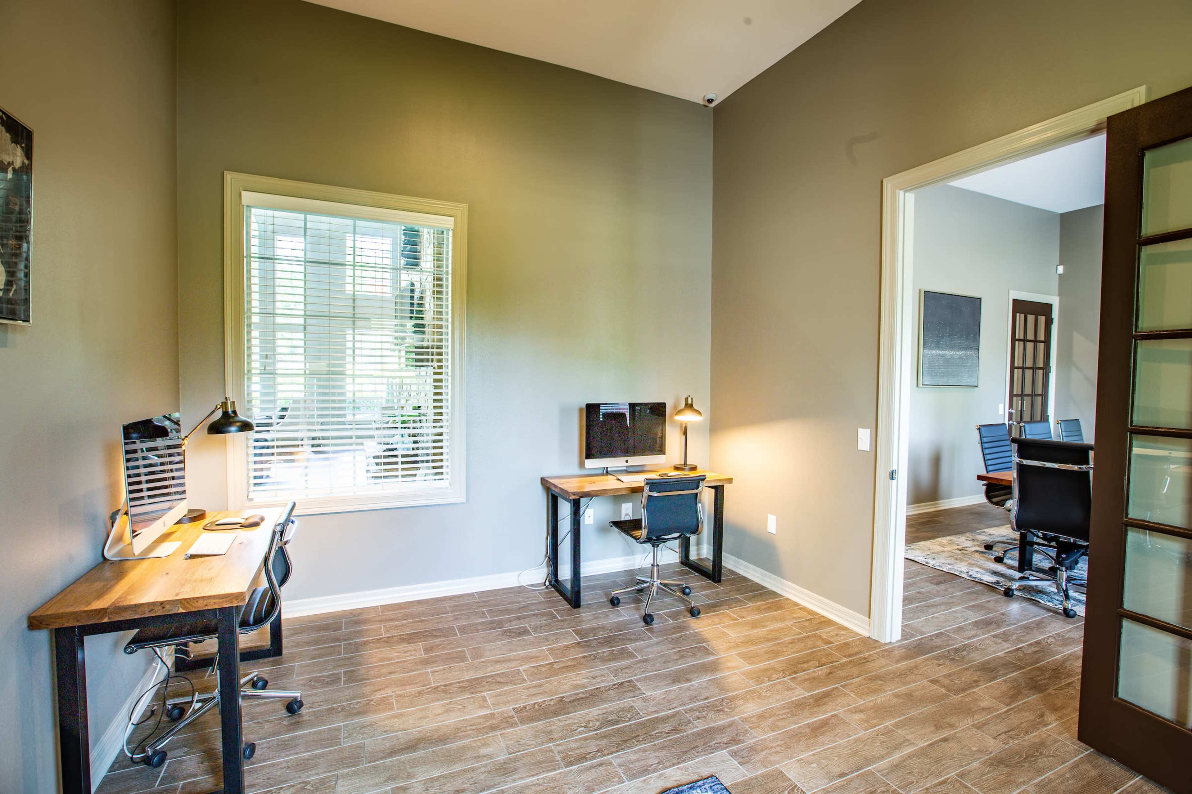 A bright office space featuring two workstations with desks and chairs, a computer on one desk, and a door leading to another room.