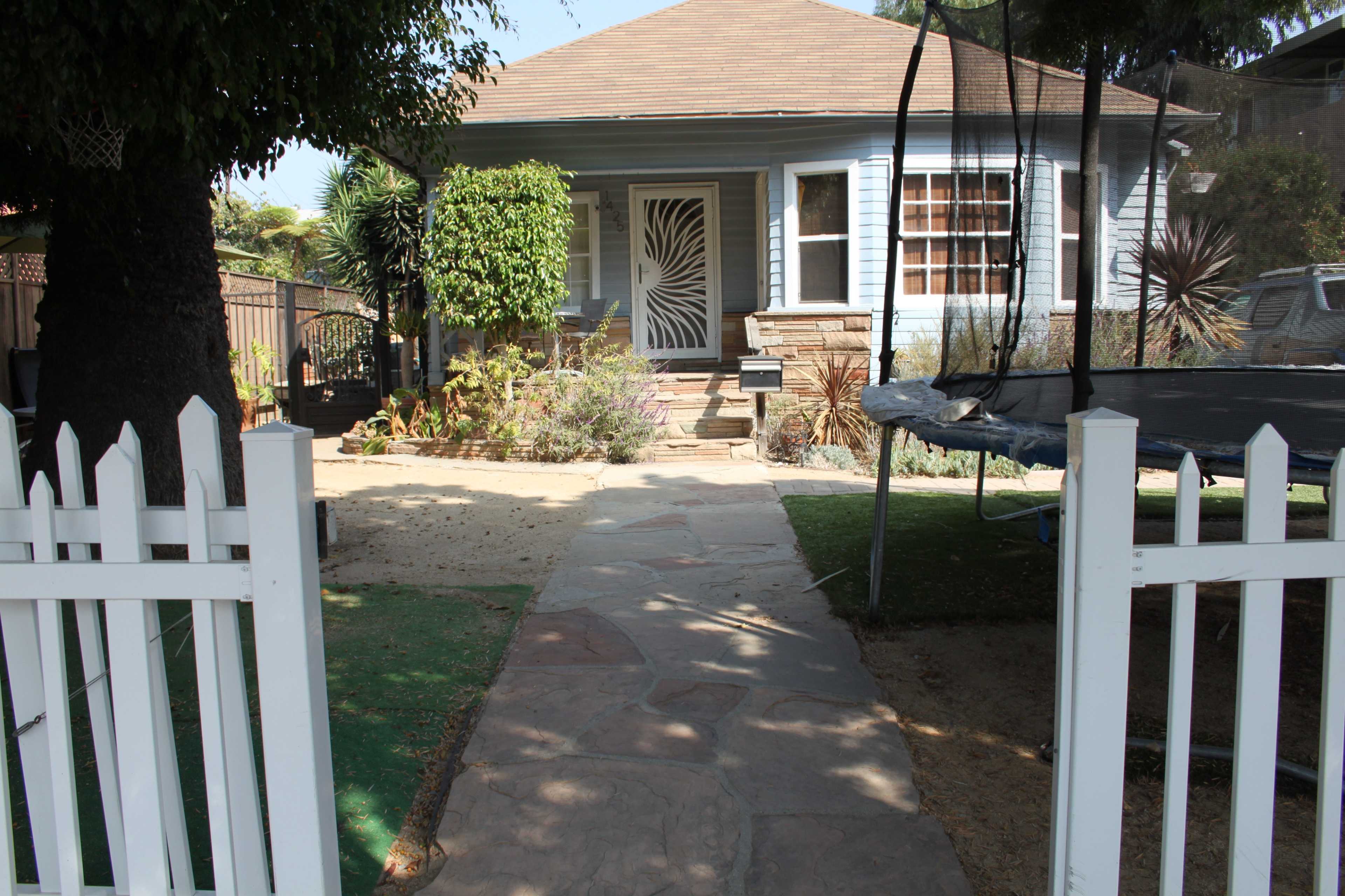 A pathway leading to a blue house with a decorative front door and a white picket fence.