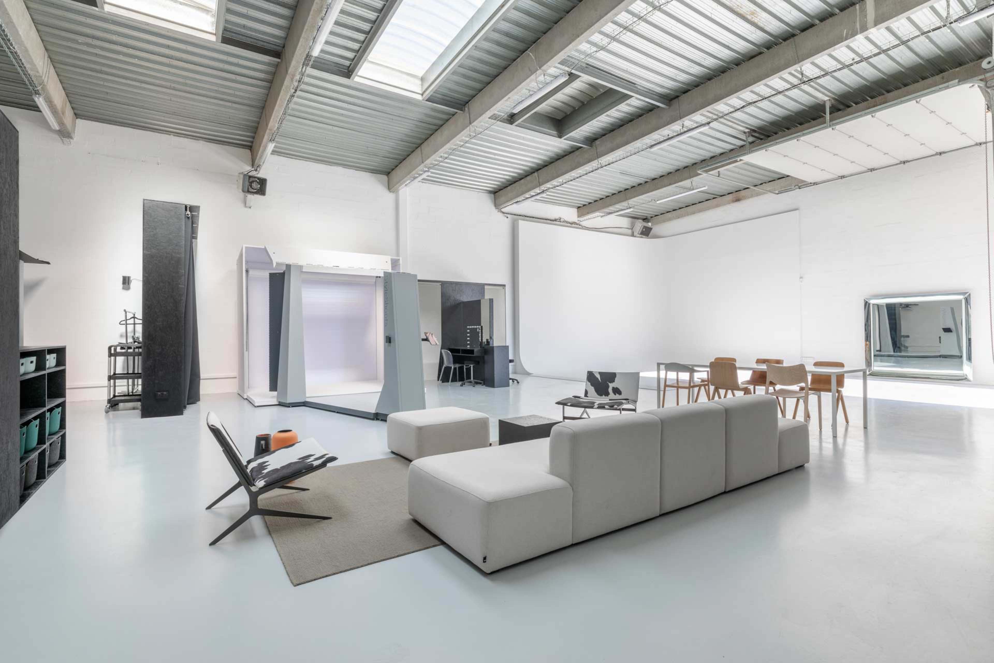 A modern open space featuring a light-colored floor, minimalistic furniture, and areas designated for relaxation and dining.
