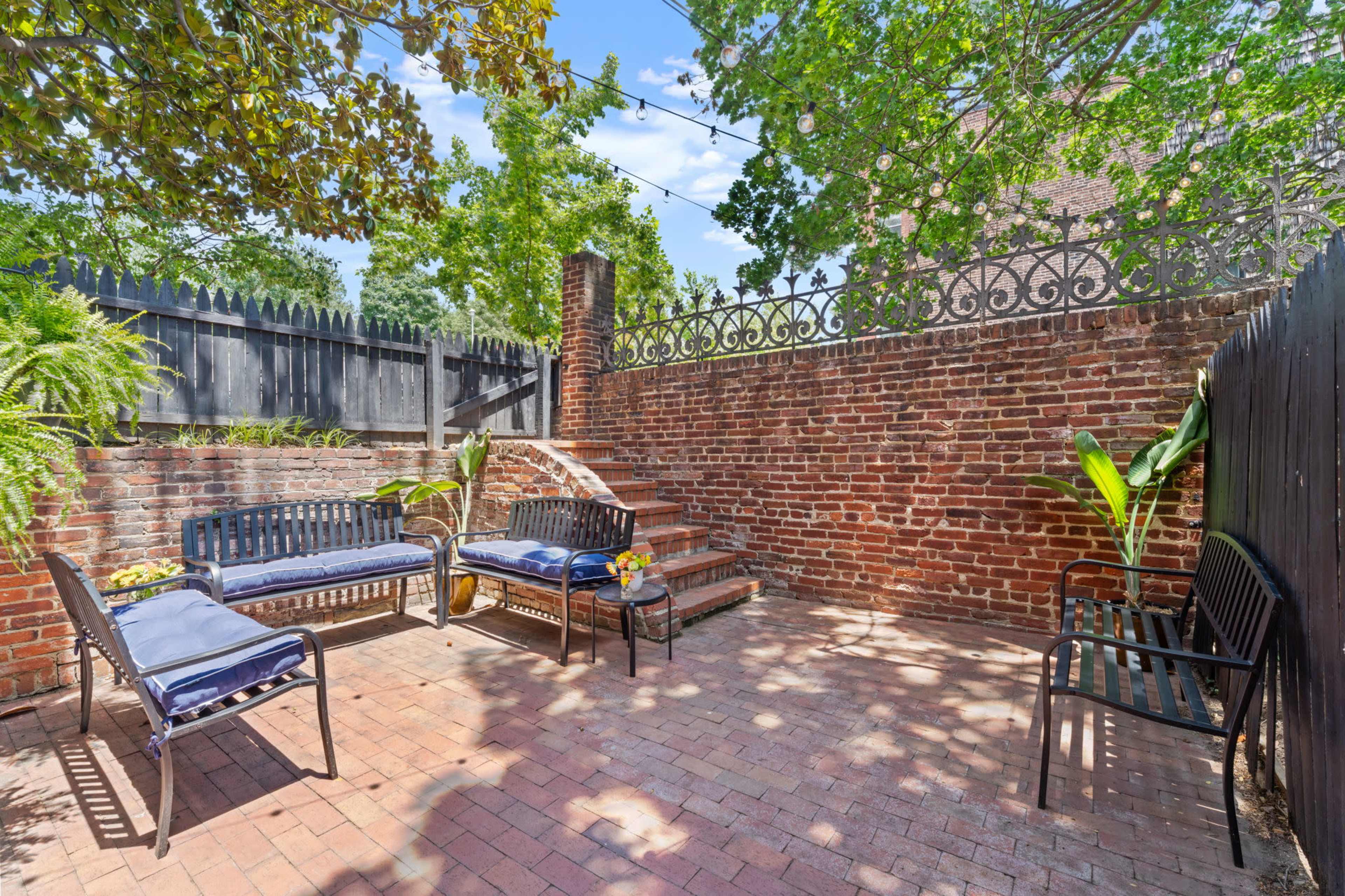 The image shows a brick patio area with several seating arrangements, surrounded by a brick wall and green foliage.