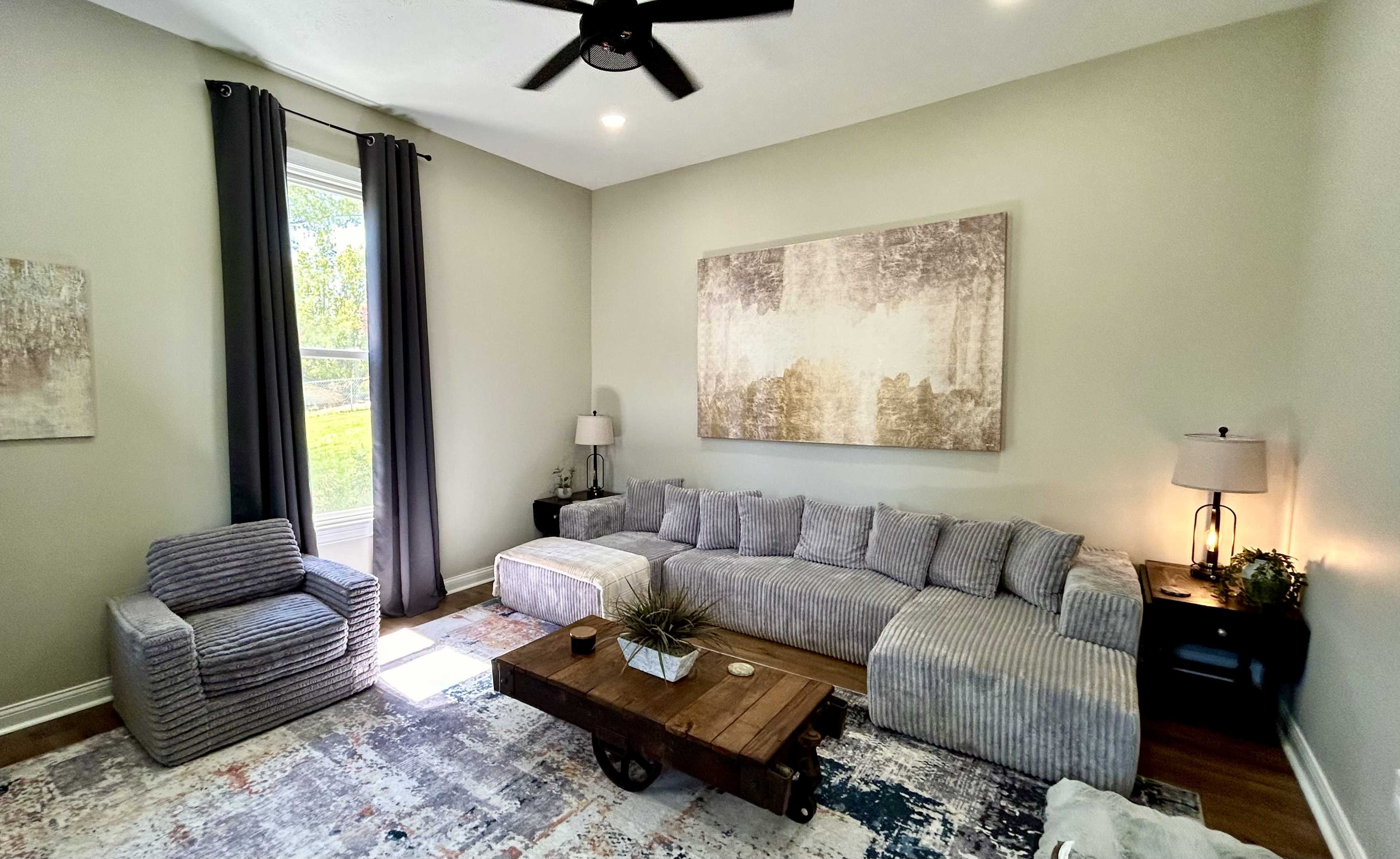 The image shows a modern living room with a sectional sofa, an accent chair, a wooden coffee table, and a large abstract painting on the wall.
