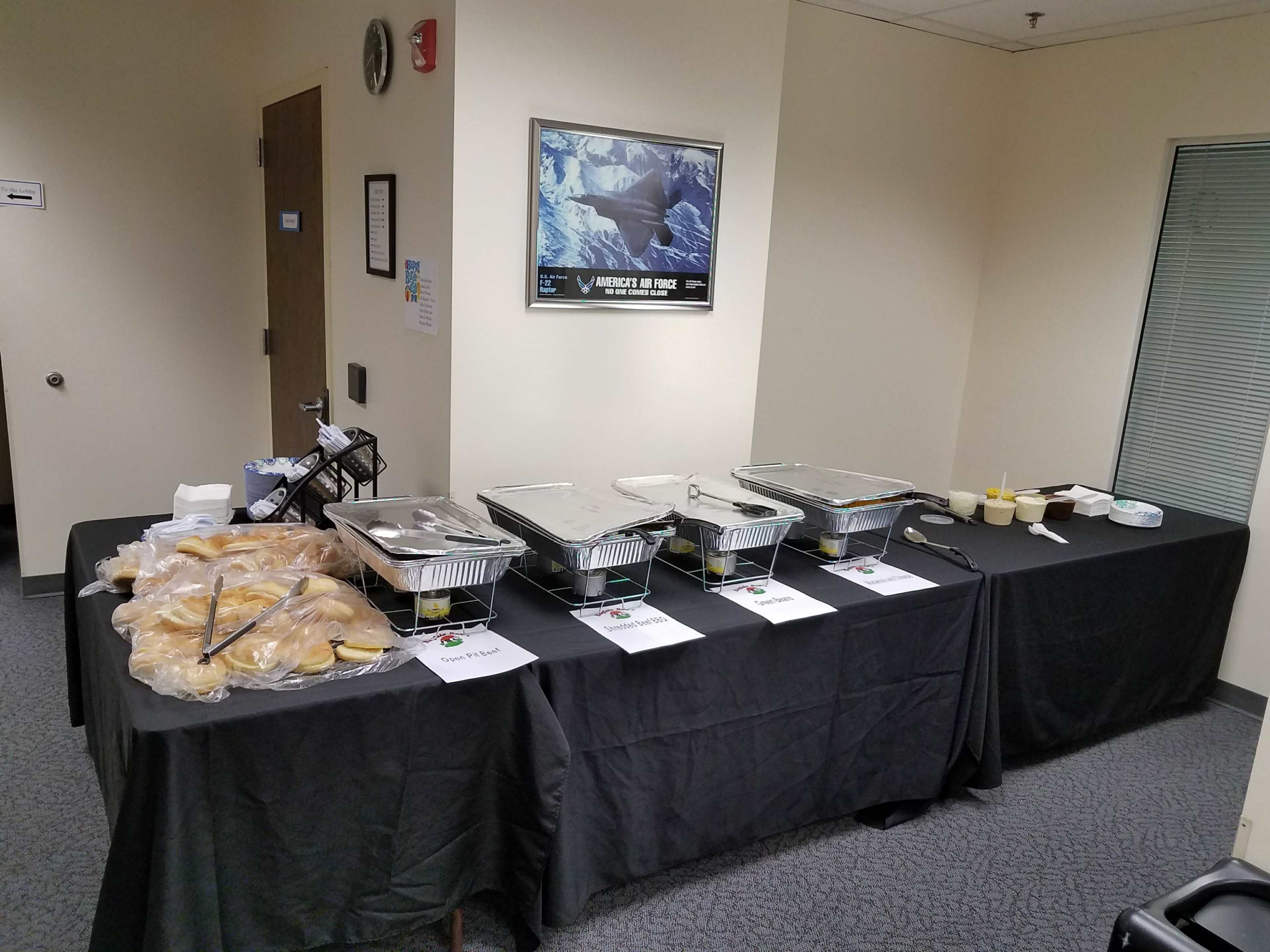 A table is set up in a room with various food containers and plates of bread arranged on a black tablecloth.