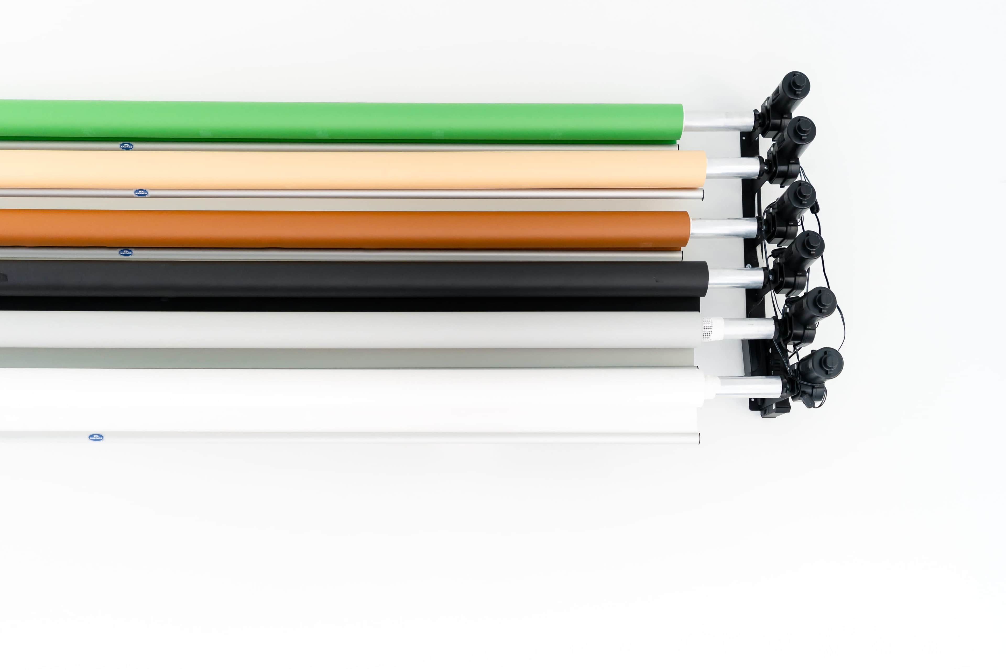 A collection of backdrop rolls in various colors, mounted on a set of black clamps against a white background.