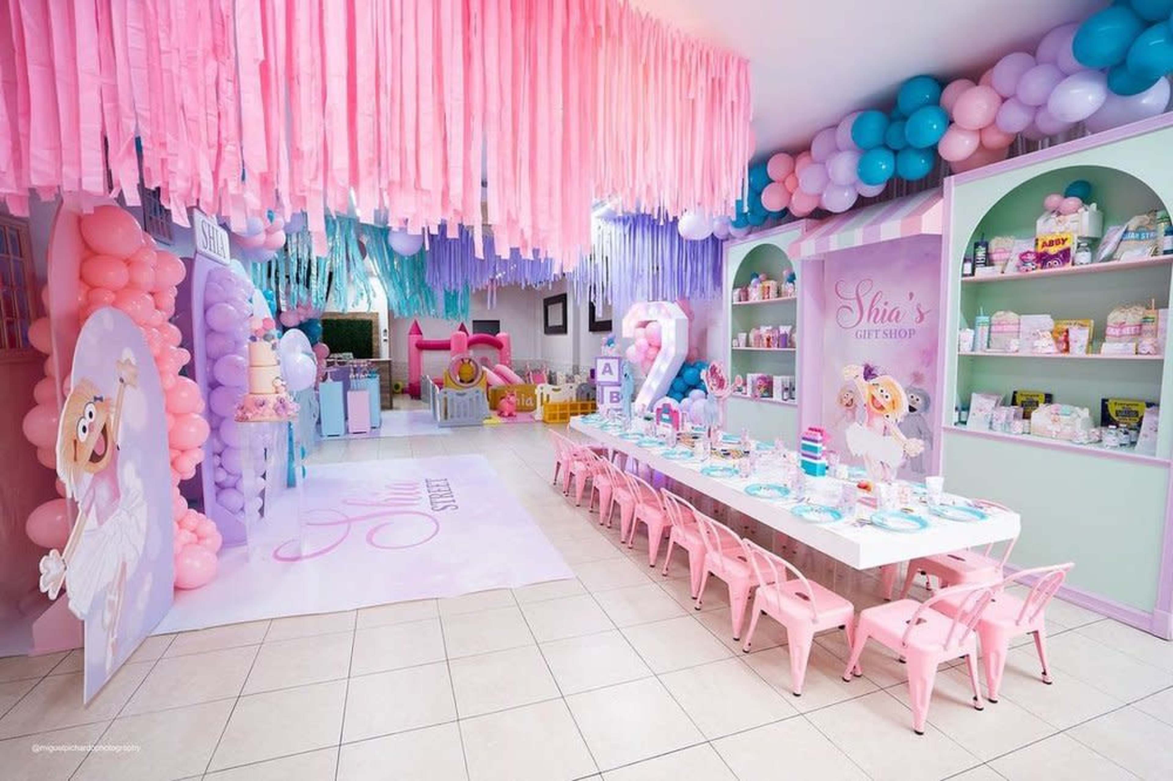 The image shows a colorful children's party space decorated with pastel balloons, streamers, and themed table settings.