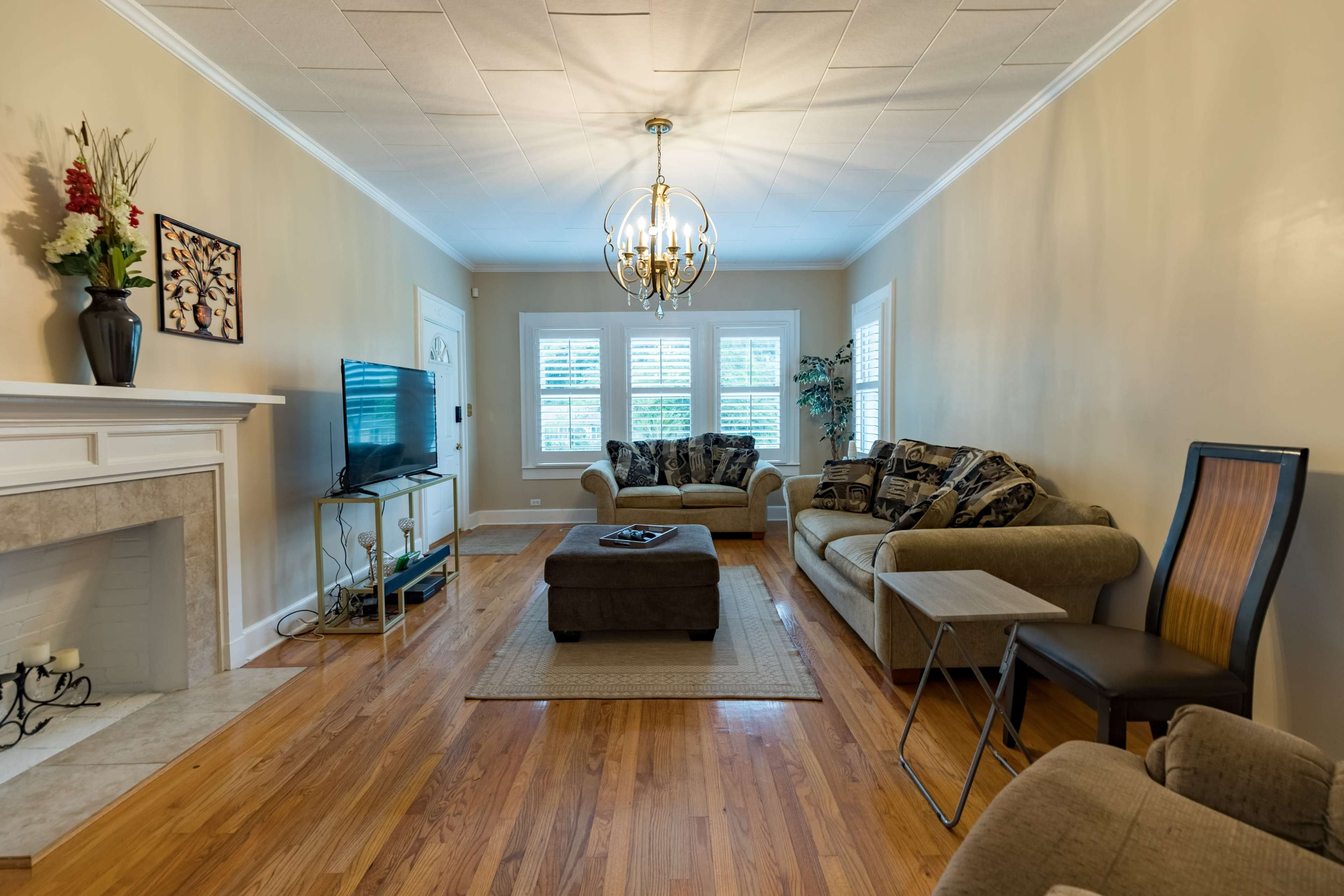 The living room features a fireplace, a television, two sofas, and a coffee table, arranged around a central area with wooden flooring.