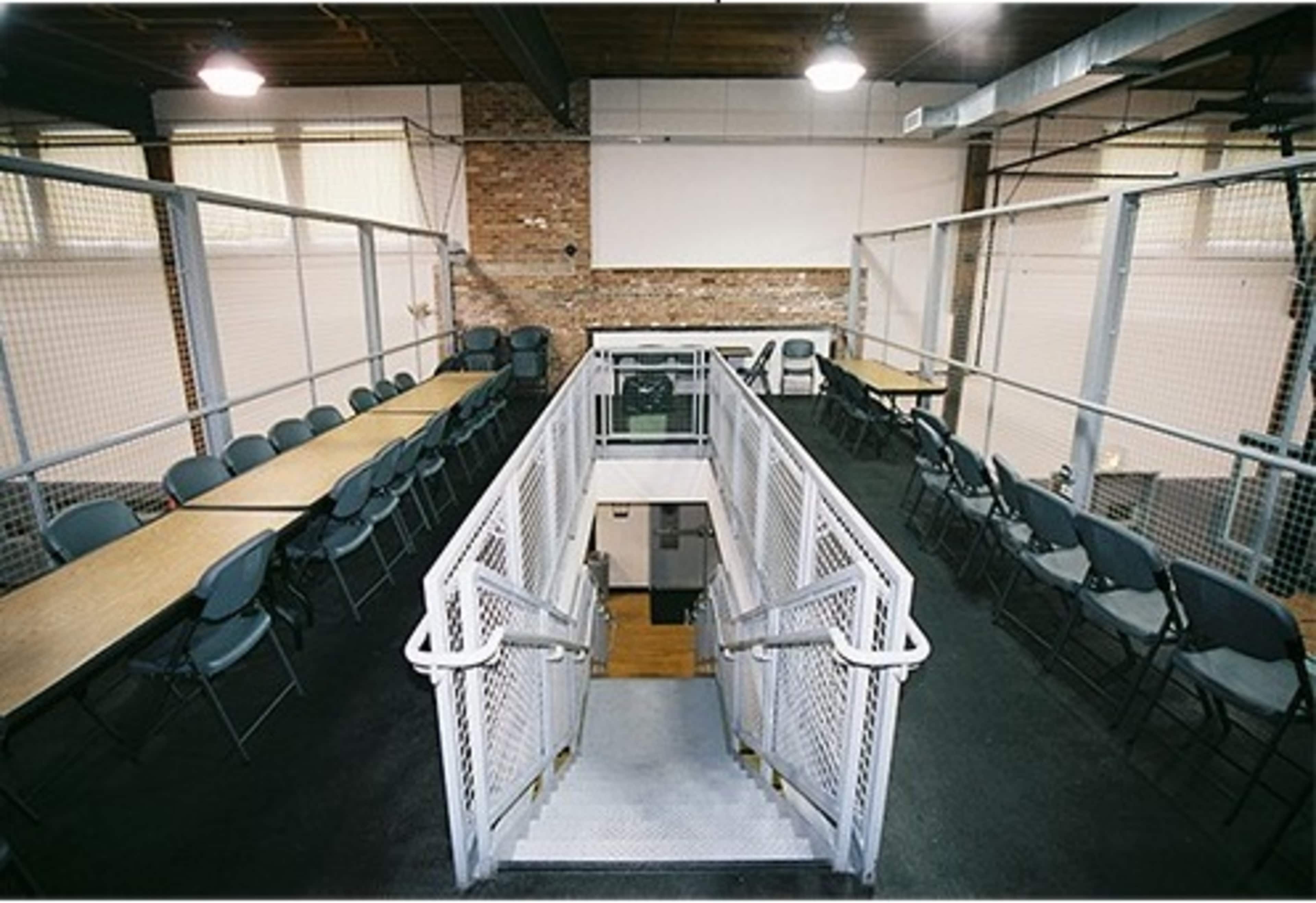 The image shows a multi-level meeting room with two long tables arranged on either side and a staircase leading down to a lower level.