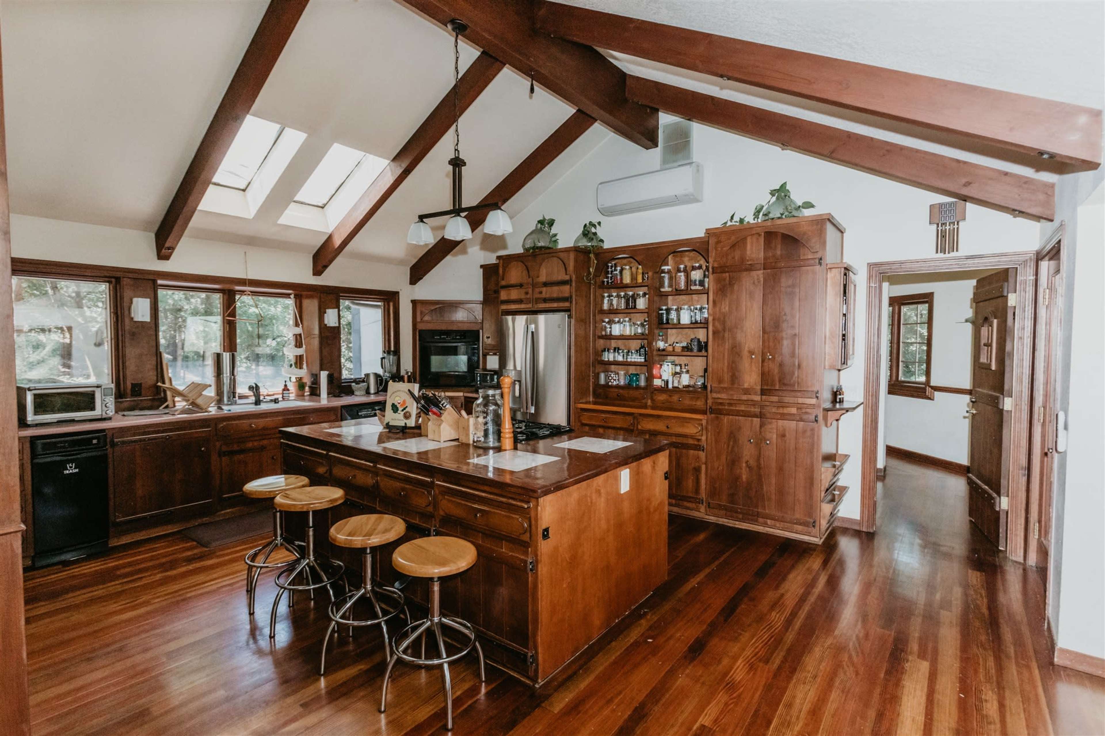 The kitchen features wooden cabinetry, a central island with seating, and skylights that illuminate the space.