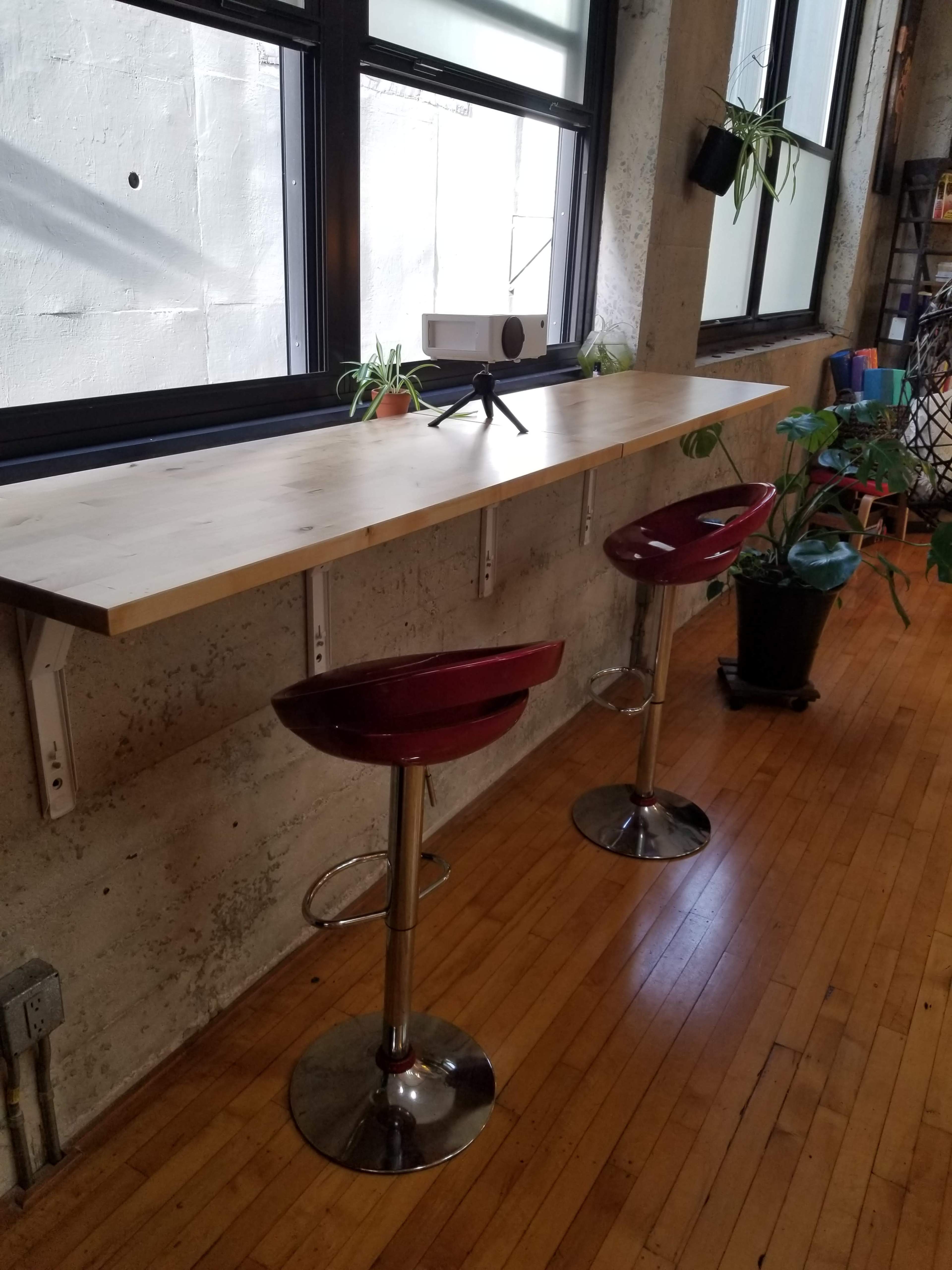 A wooden countertop extends against a window, accompanied by two red bar stools and potted plants.