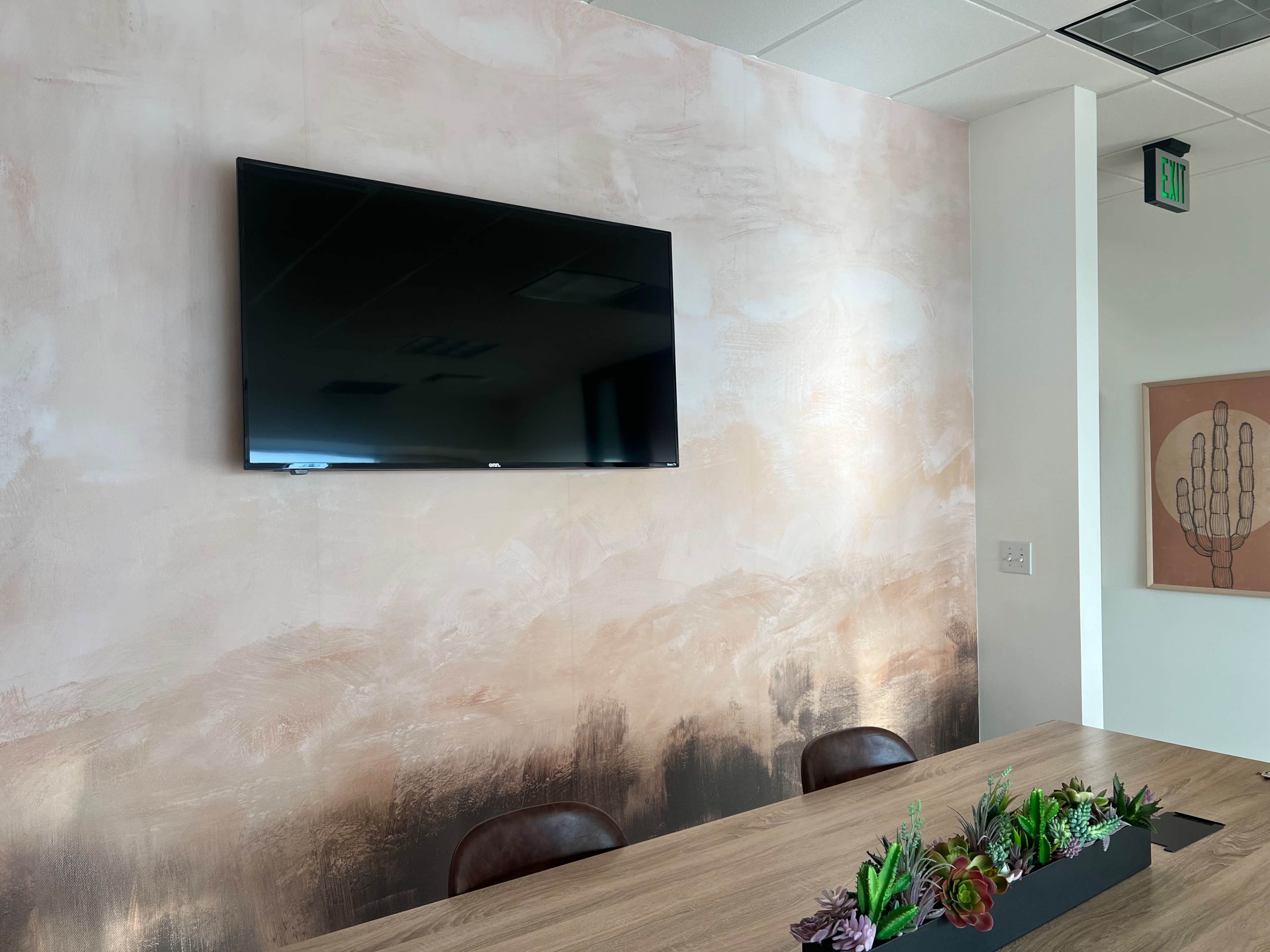 A modern conference room with a wall-mounted television above a wooden table adorned with a planter of succulents.