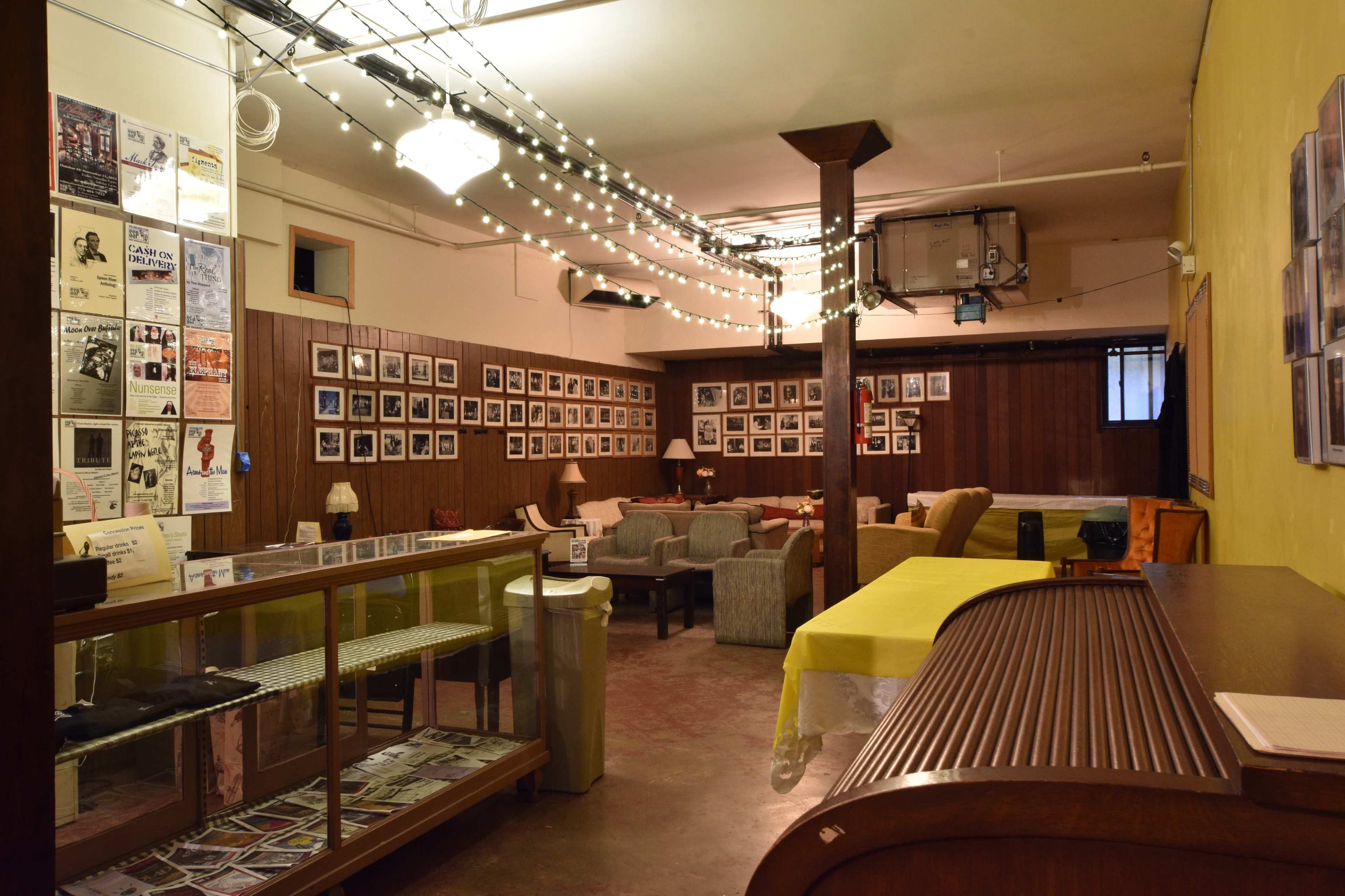 A cozy lounge area with framed photographs and posters on the walls, string lights overhead, and seating arranged around a central space.