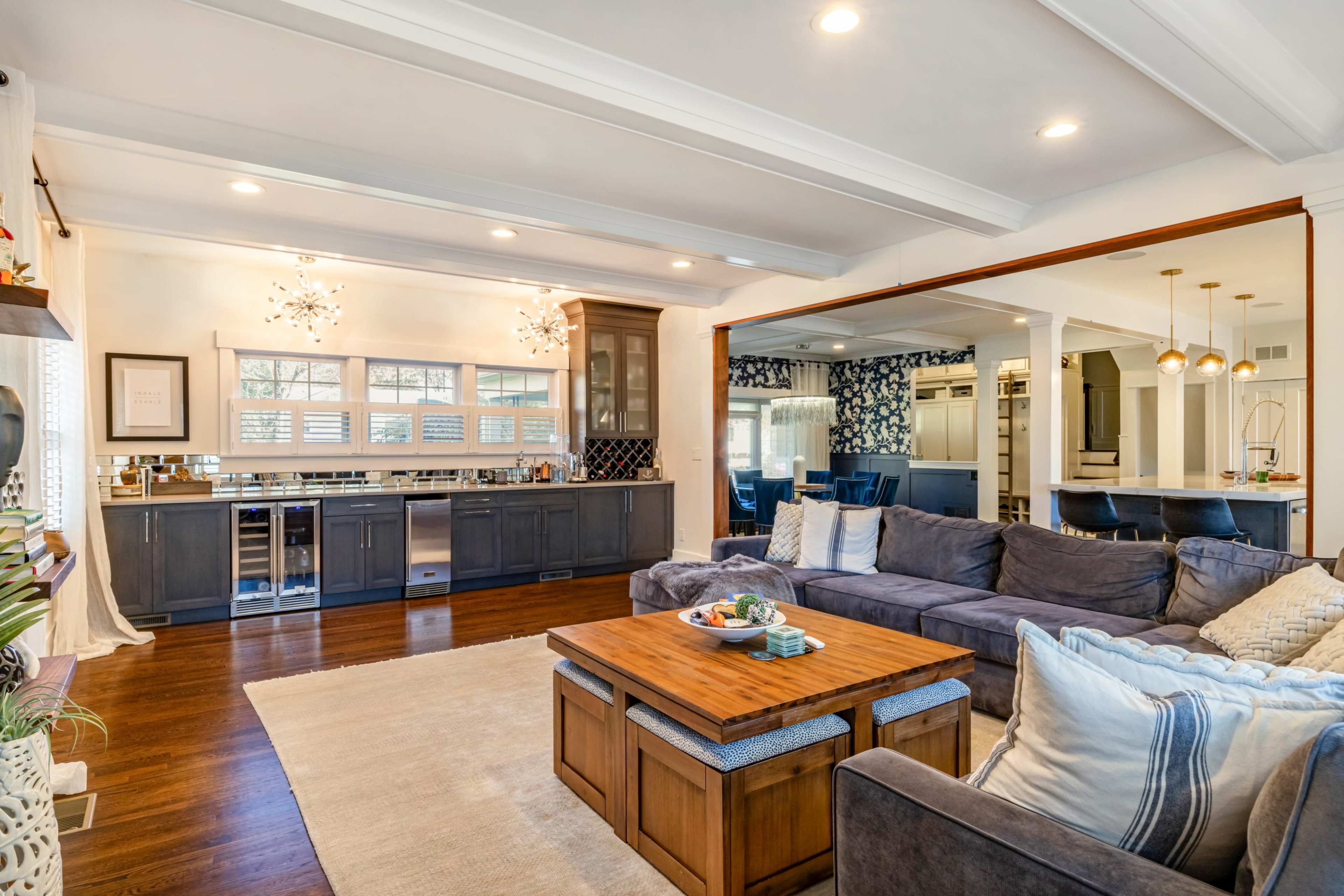 The image shows a spacious living room with a dark sectional sofa, a wooden coffee table, and an open kitchen area featuring modern cabinetry and fixtures.