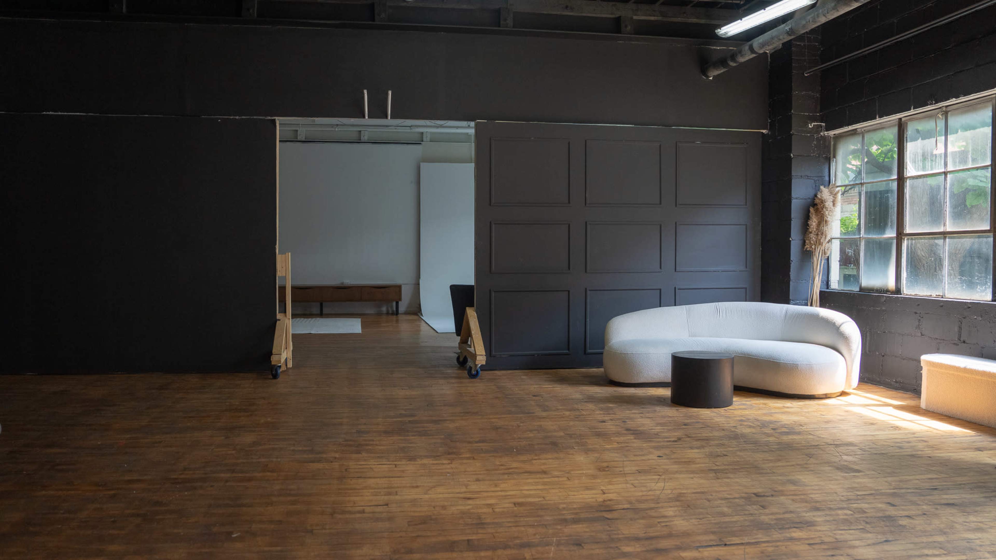 A spacious indoor area features a dark wall with sliding doors leading to a lighter room, and various modern furniture pieces are arranged throughout.