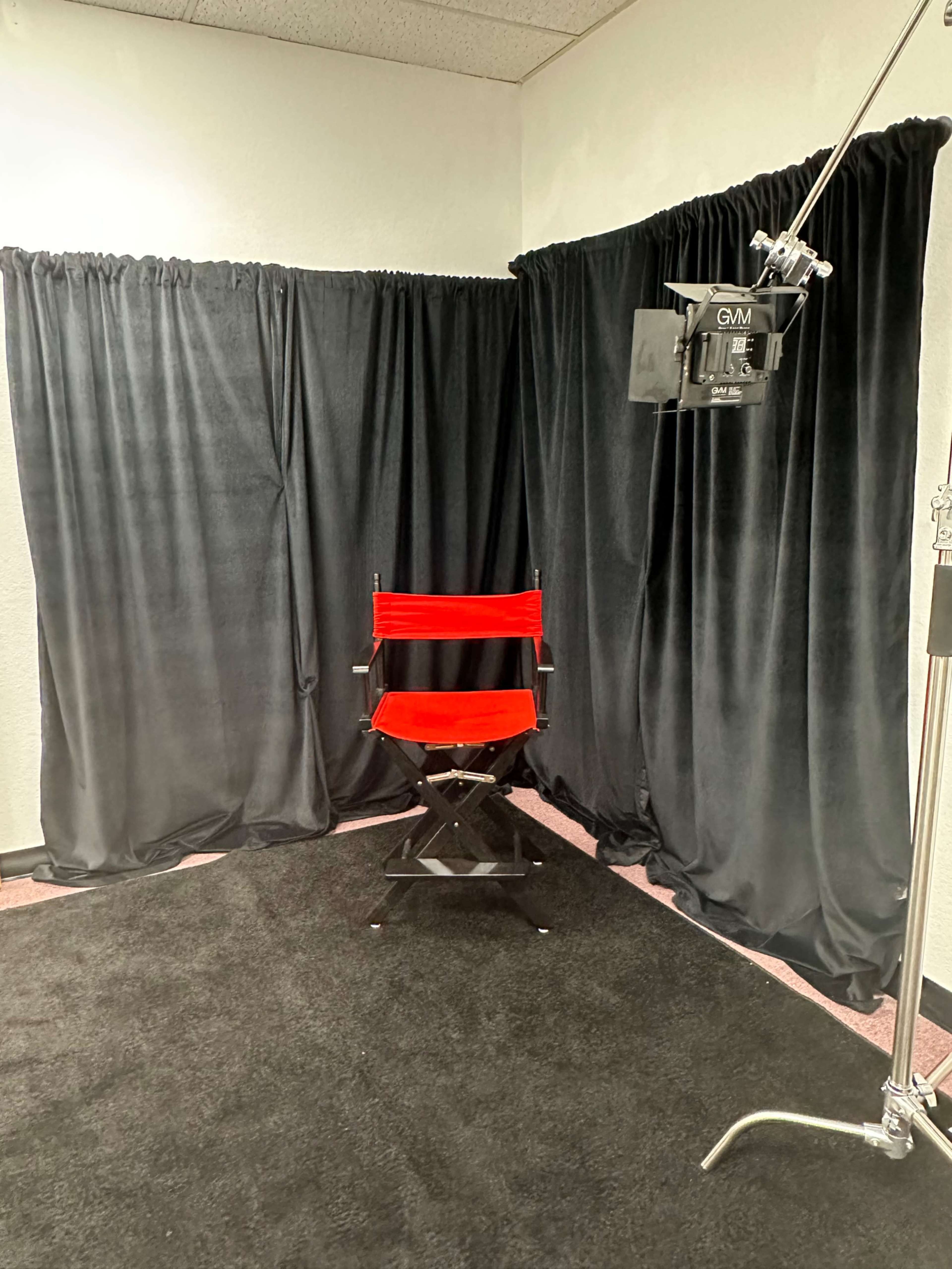A red director's chair positioned in a corner surrounded by black curtains and a black carpet.