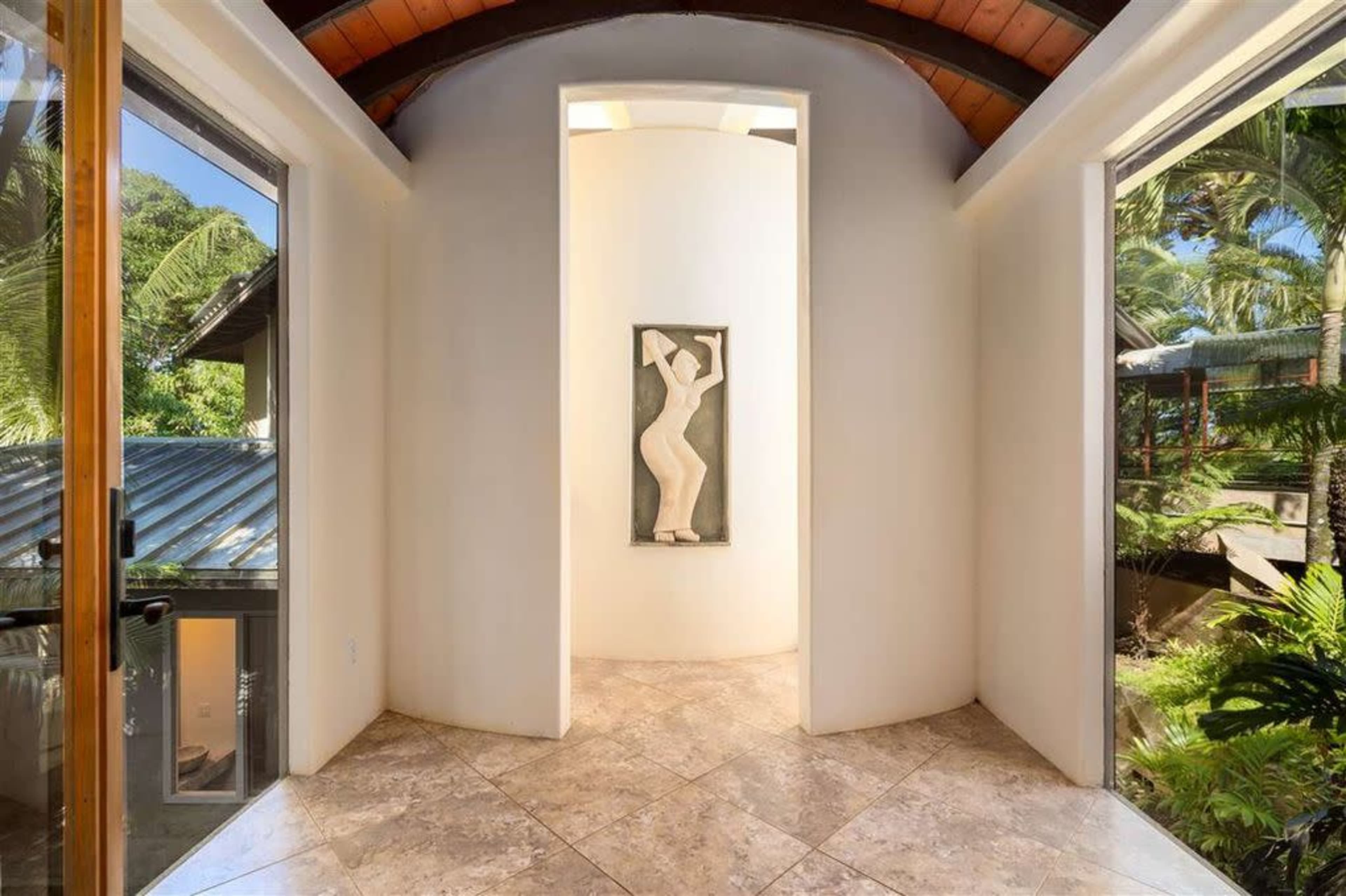 A rounded hallway with a central sculpture and large windows that provide views of the surrounding greenery.