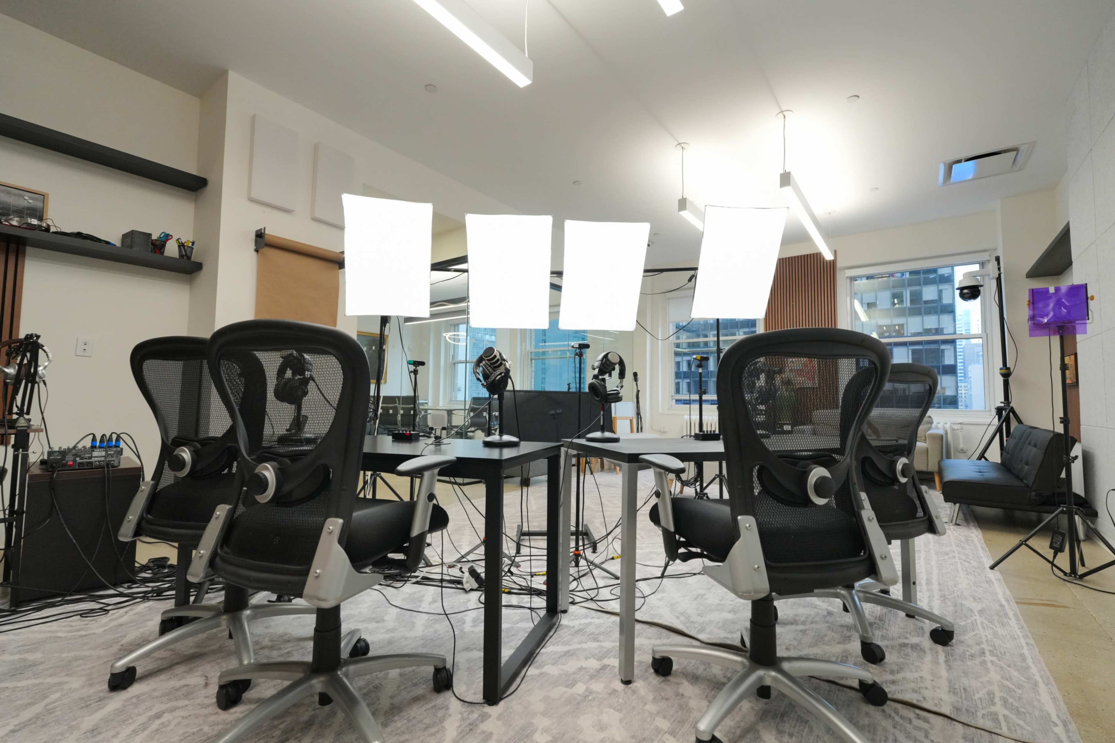 A modern workspace is set up with multiple chairs facing a table, surrounded by lighting equipment and various cables.