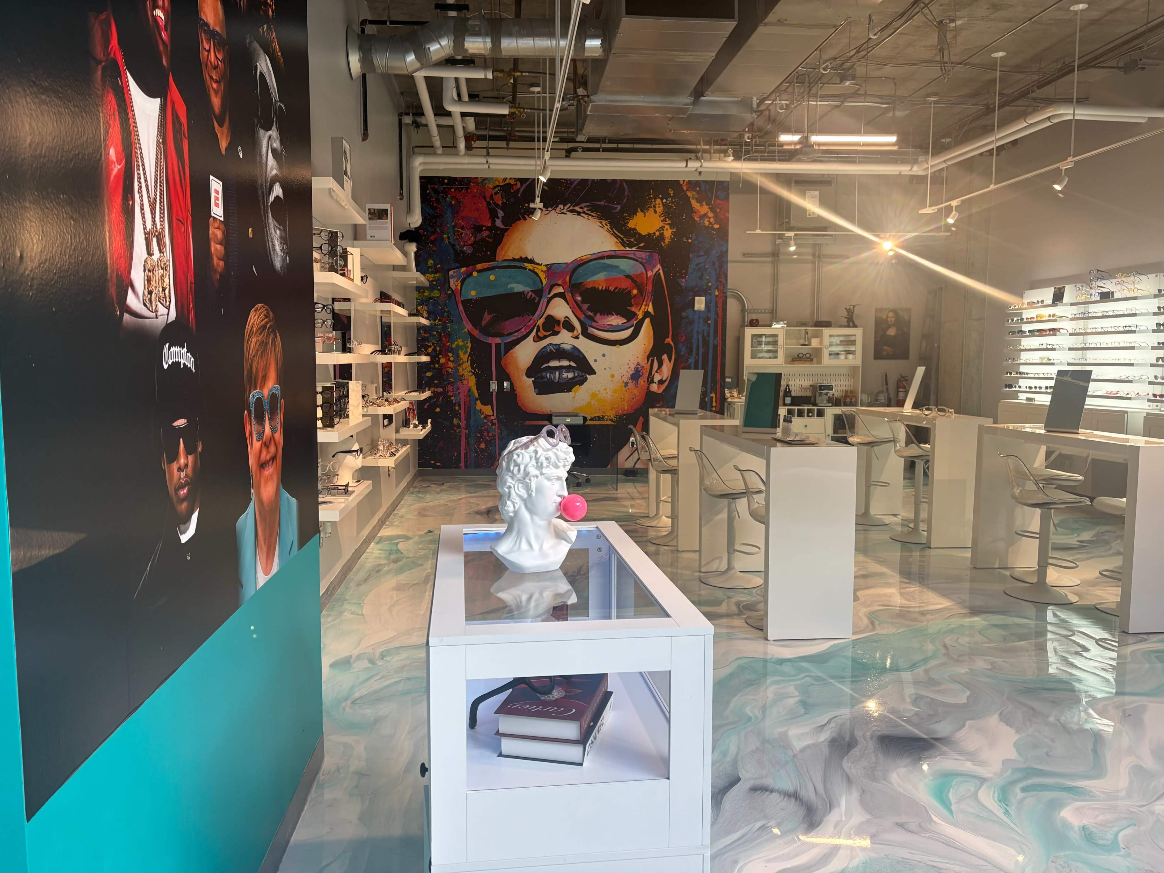 The image shows a modern retail space featuring artistic wall murals, display shelves, and a bright, swirled floor design.