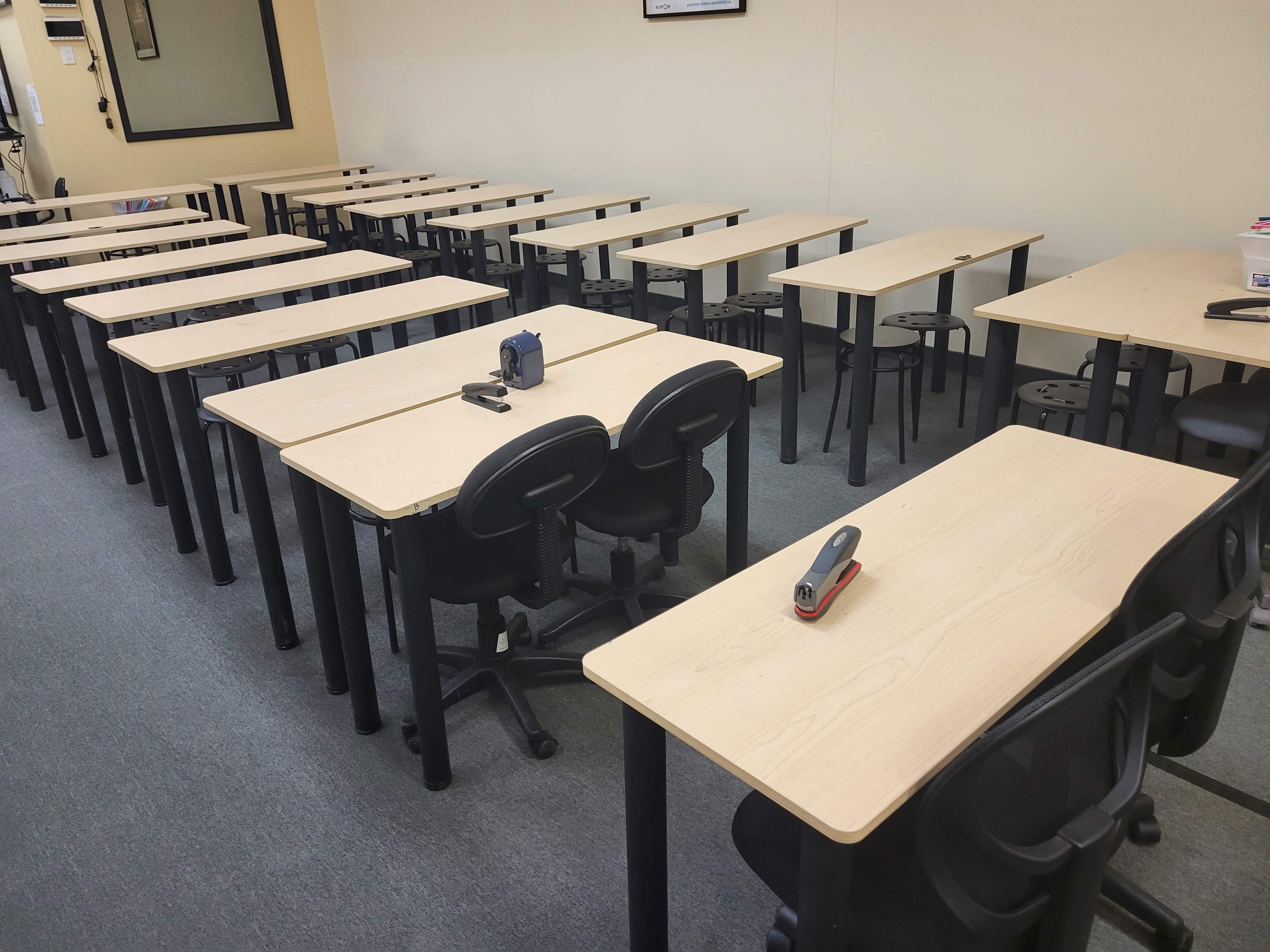 A classroom with multiple rows of empty tables and chairs arranged in a structured layout.