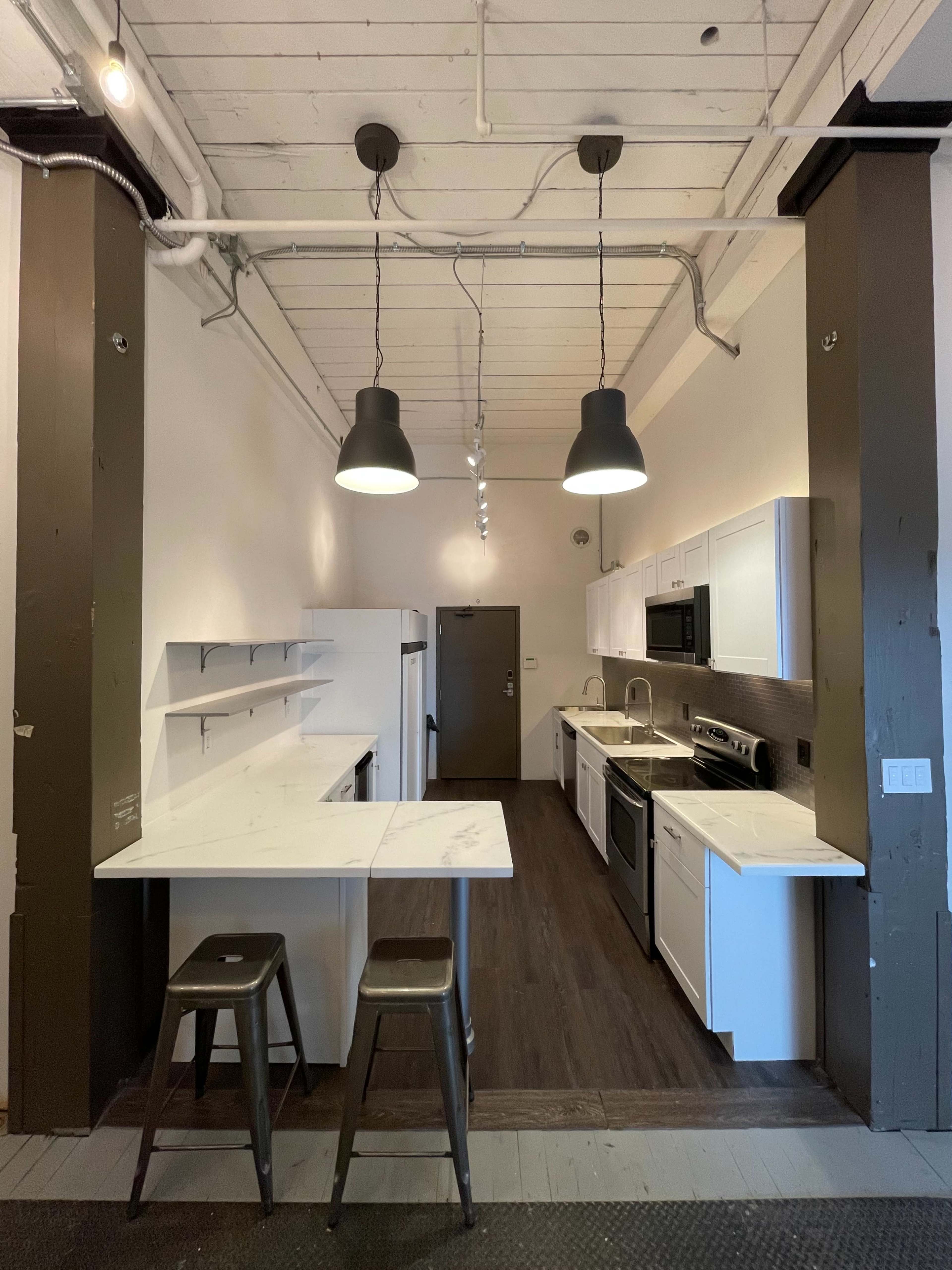 A modern kitchen with white cabinets, stainless steel appliances, and two metal stools situated at a small breakfast bar.