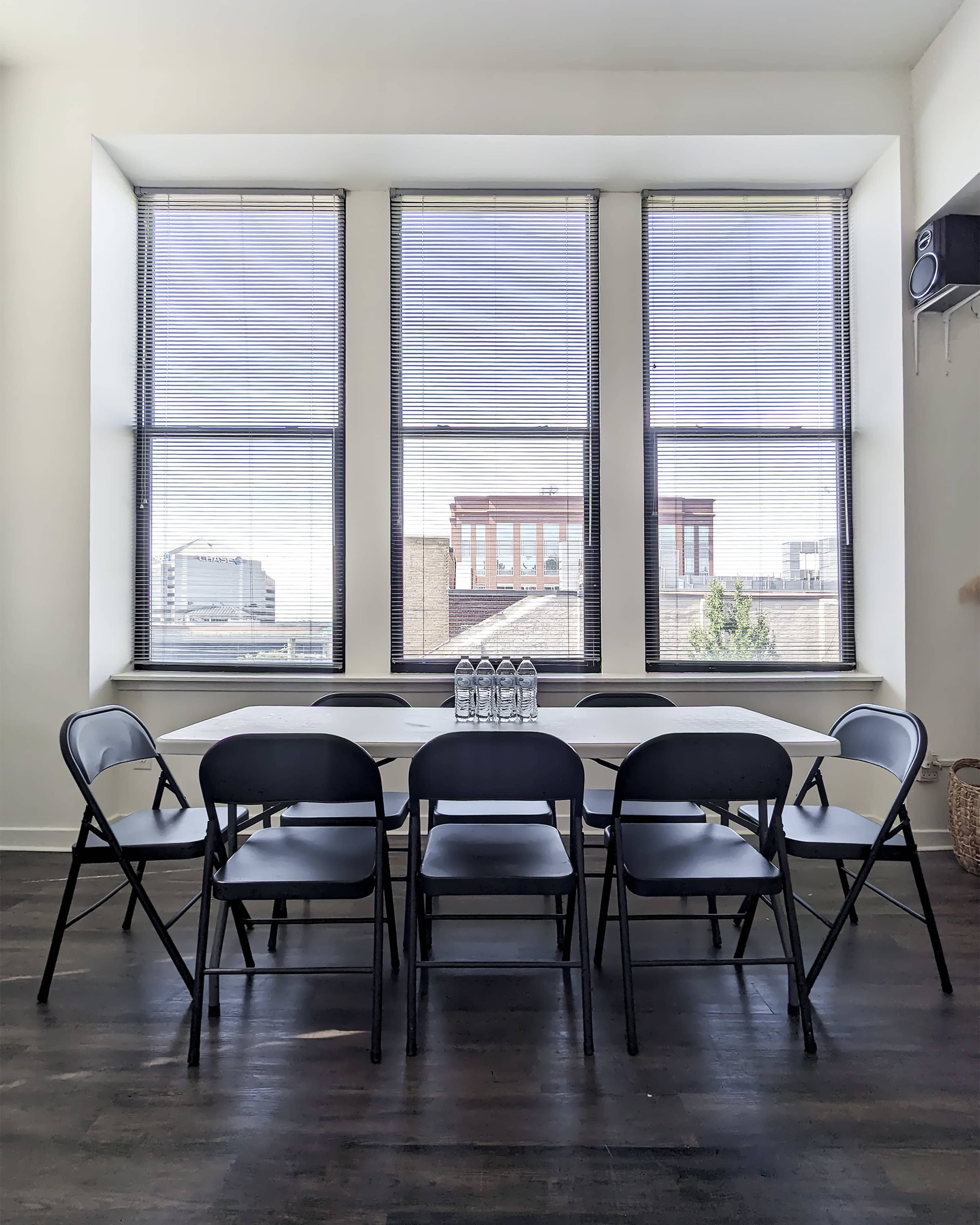 A long table with six black chairs is positioned in front of large windows overlooking a cityscape.