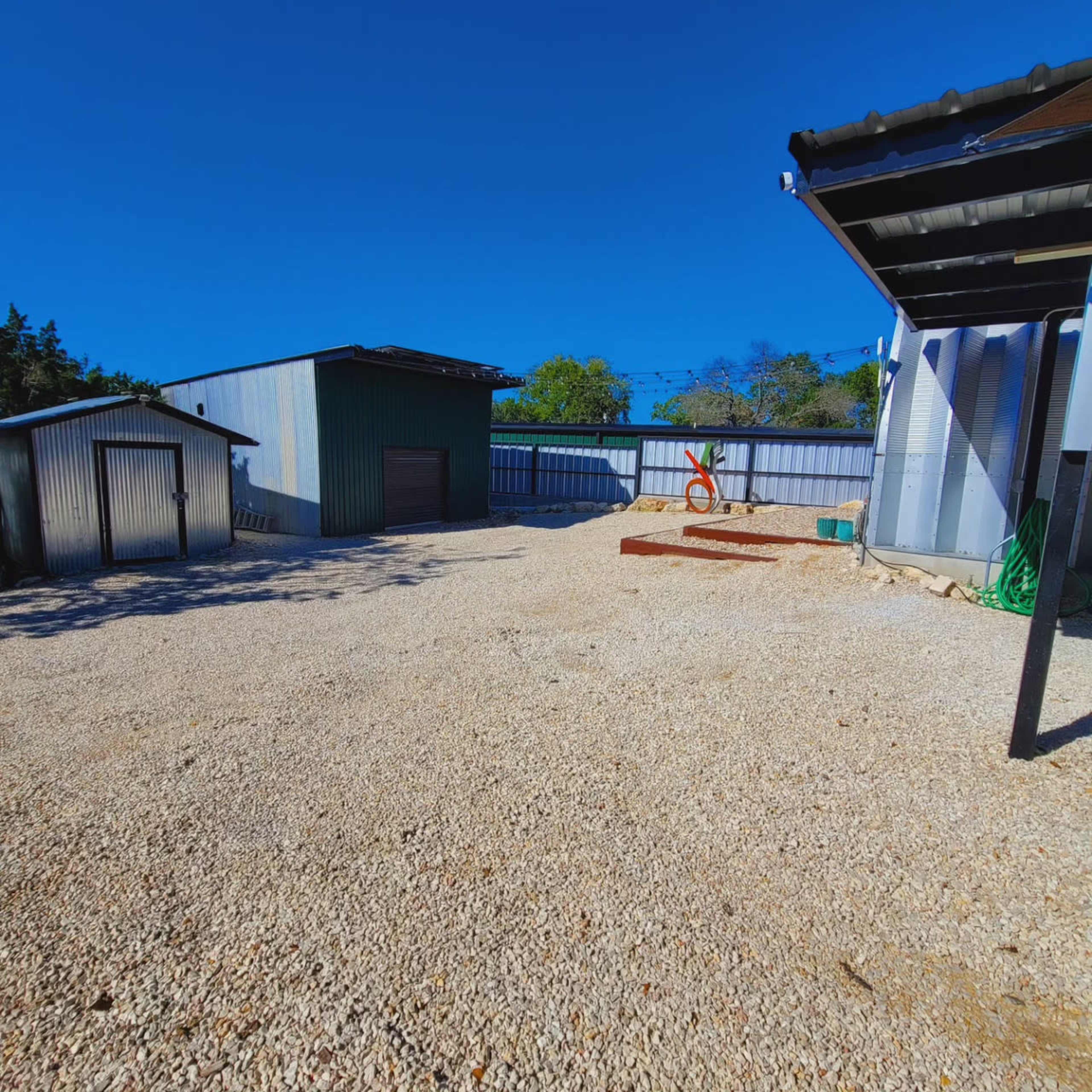 A gravel-covered area with several metal buildings and a wooden structure under a clear blue sky.