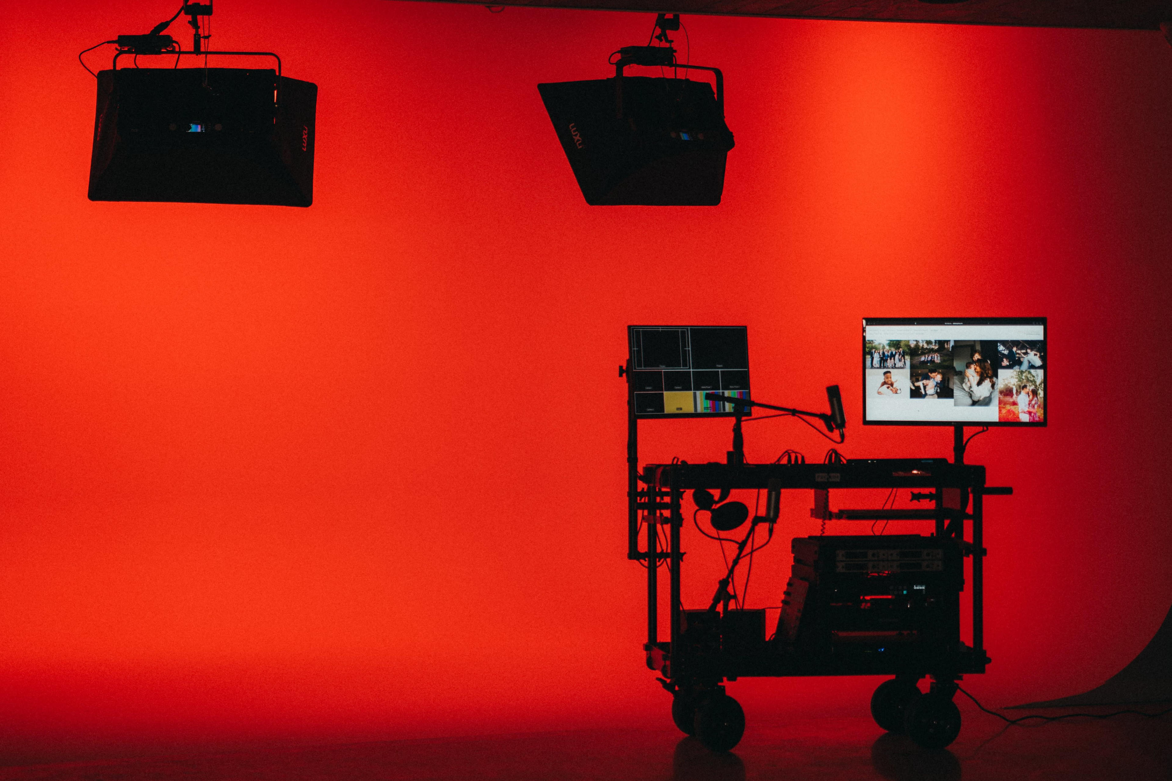 A studio setup with two overhead lights and a computer monitor displaying images, against a red backdrop.