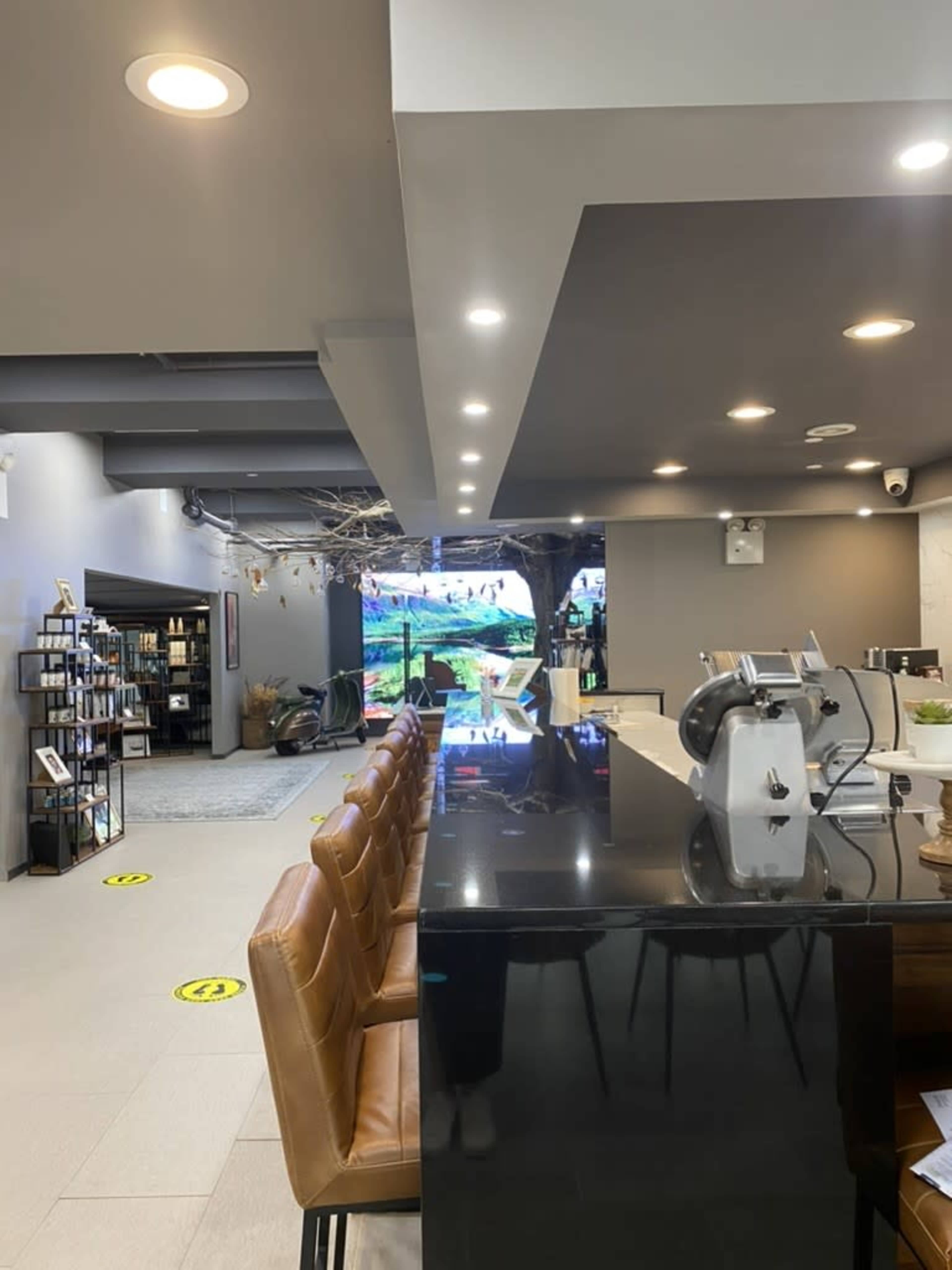 A modern interior features a dark countertop bar with brown leather stools, leading to a display area with greenery and a large screen in the background.