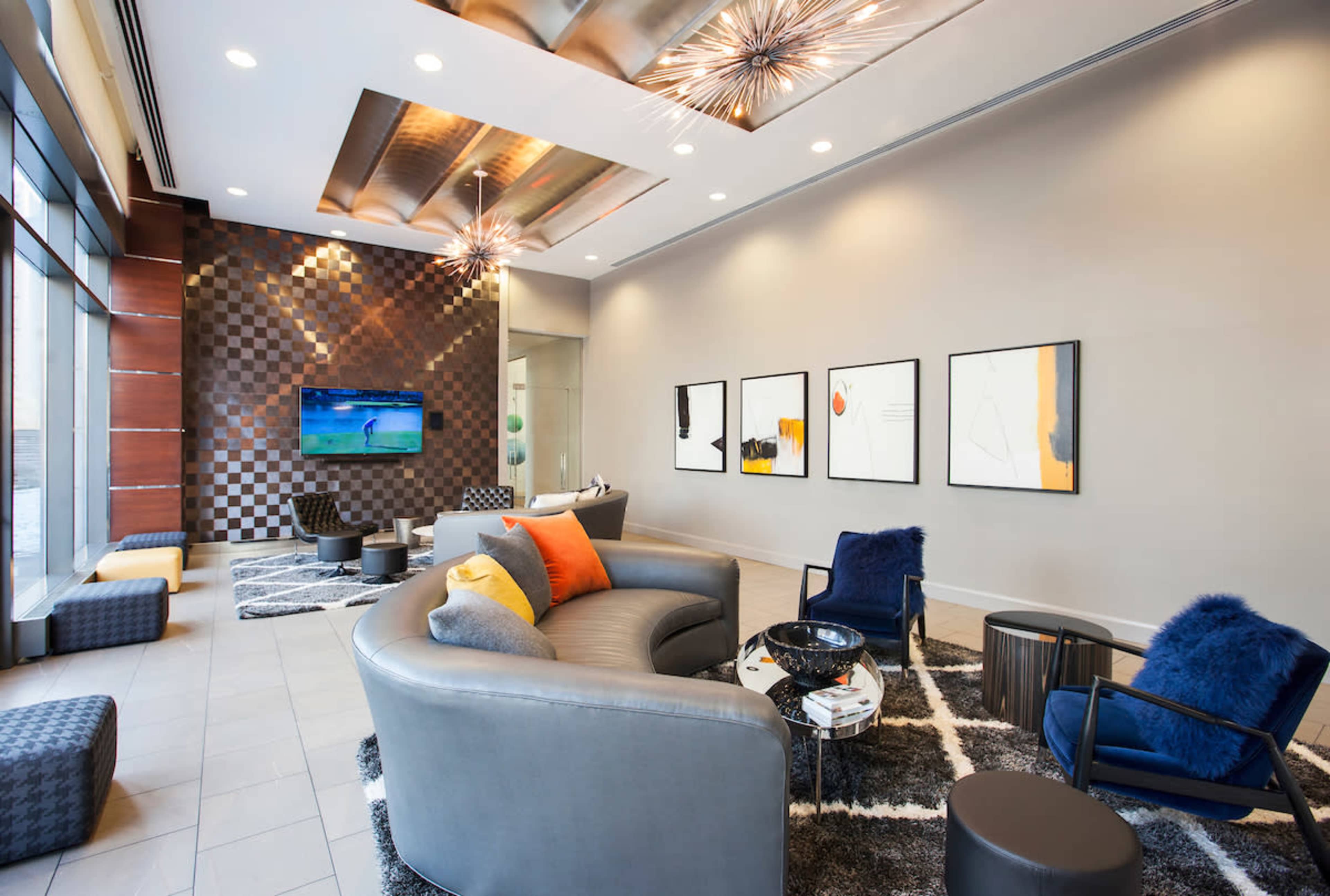 The image shows a modern lounge area with a textured wall, comfortable seating, and a television mounted on a checkered background.