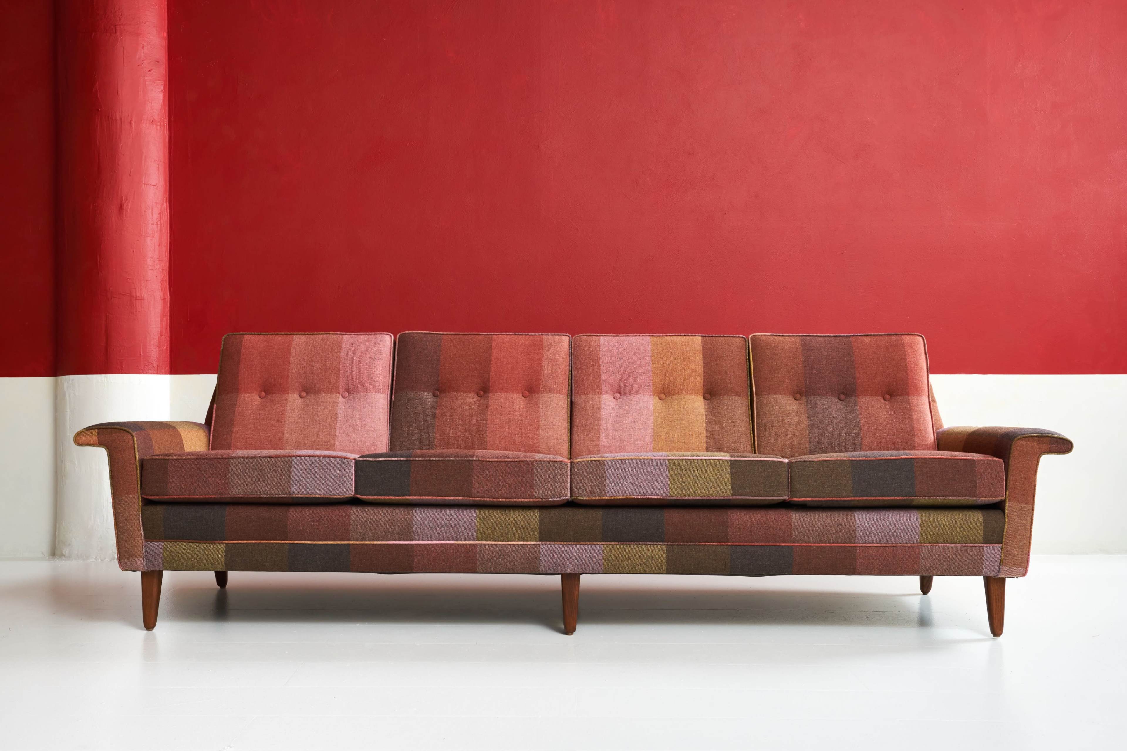 A multicolored plaid sofa with wooden legs sits against a red wall with a white lower section.